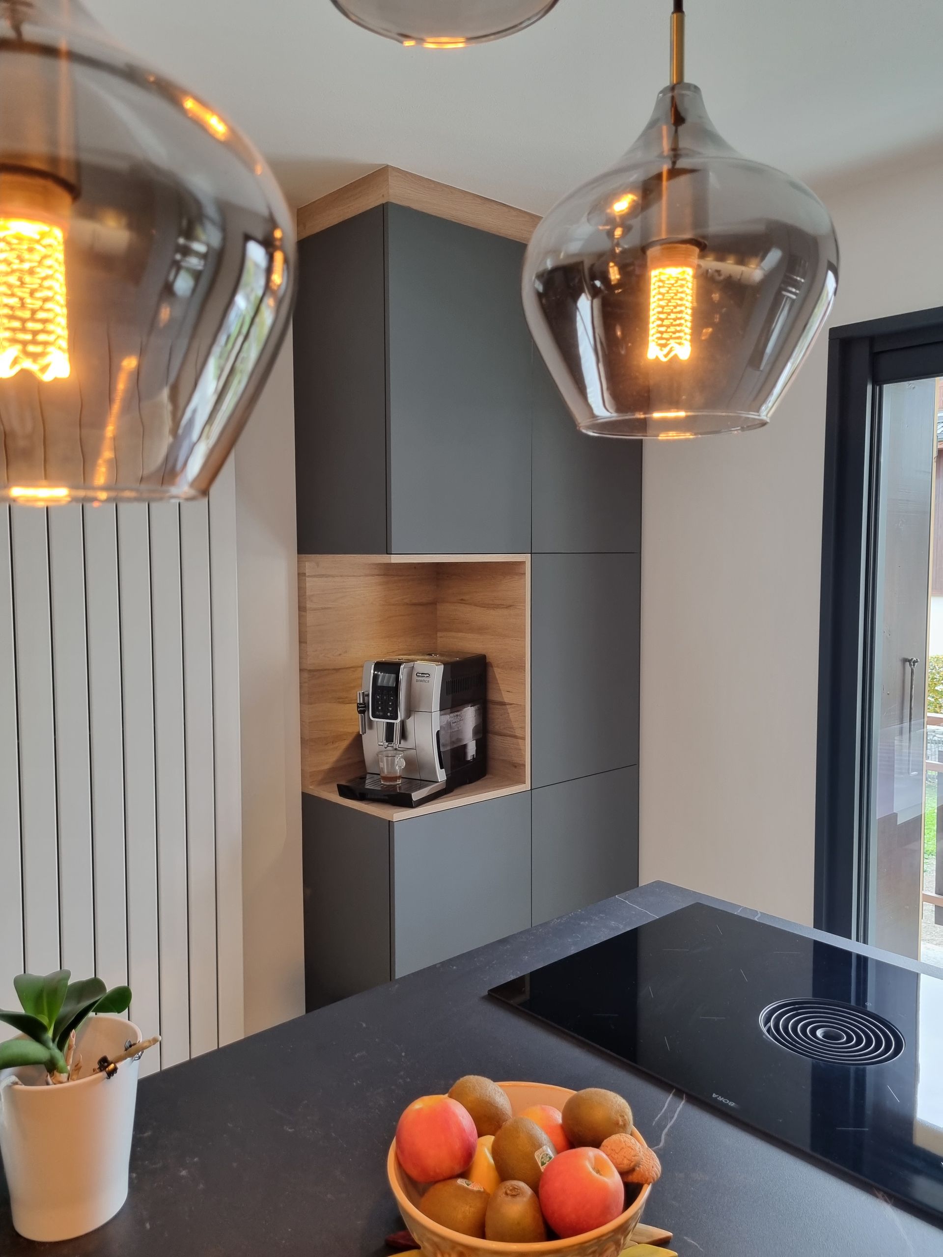 Cuisine moderne avec placards gris, éléments en bois, suspensions lumineuses et coin café intégré.