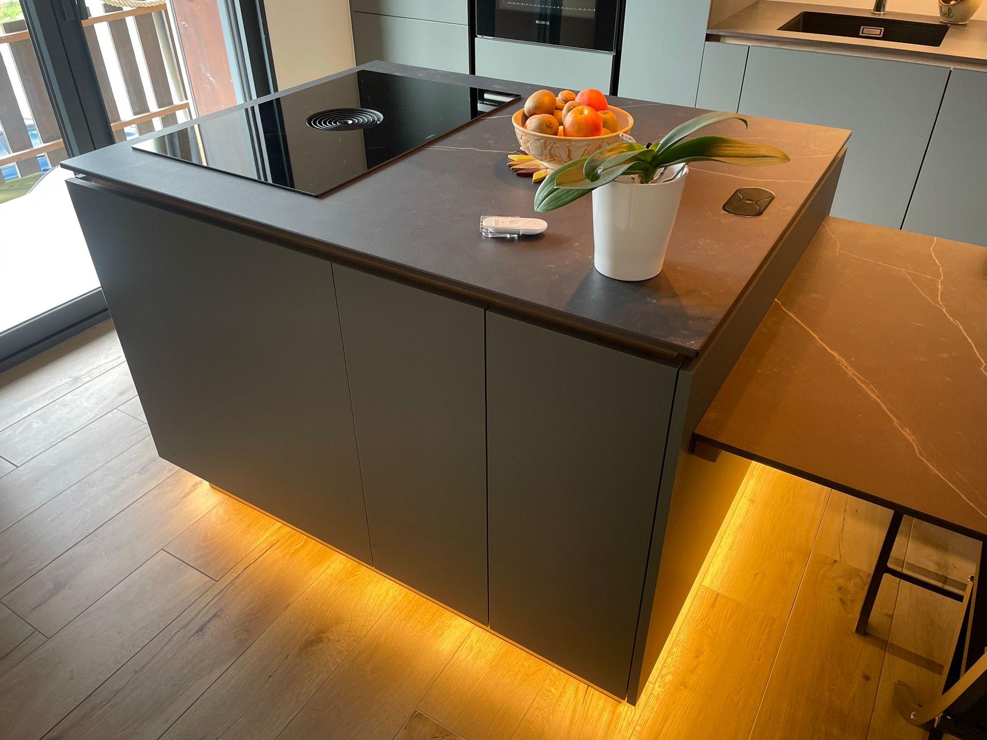 Îlot de cuisine moderne avec plaque de cuisson, corbeille à fruits et extension de comptoir coulissante ; armoires grises, éclairage chaleureux sous les armoires.
