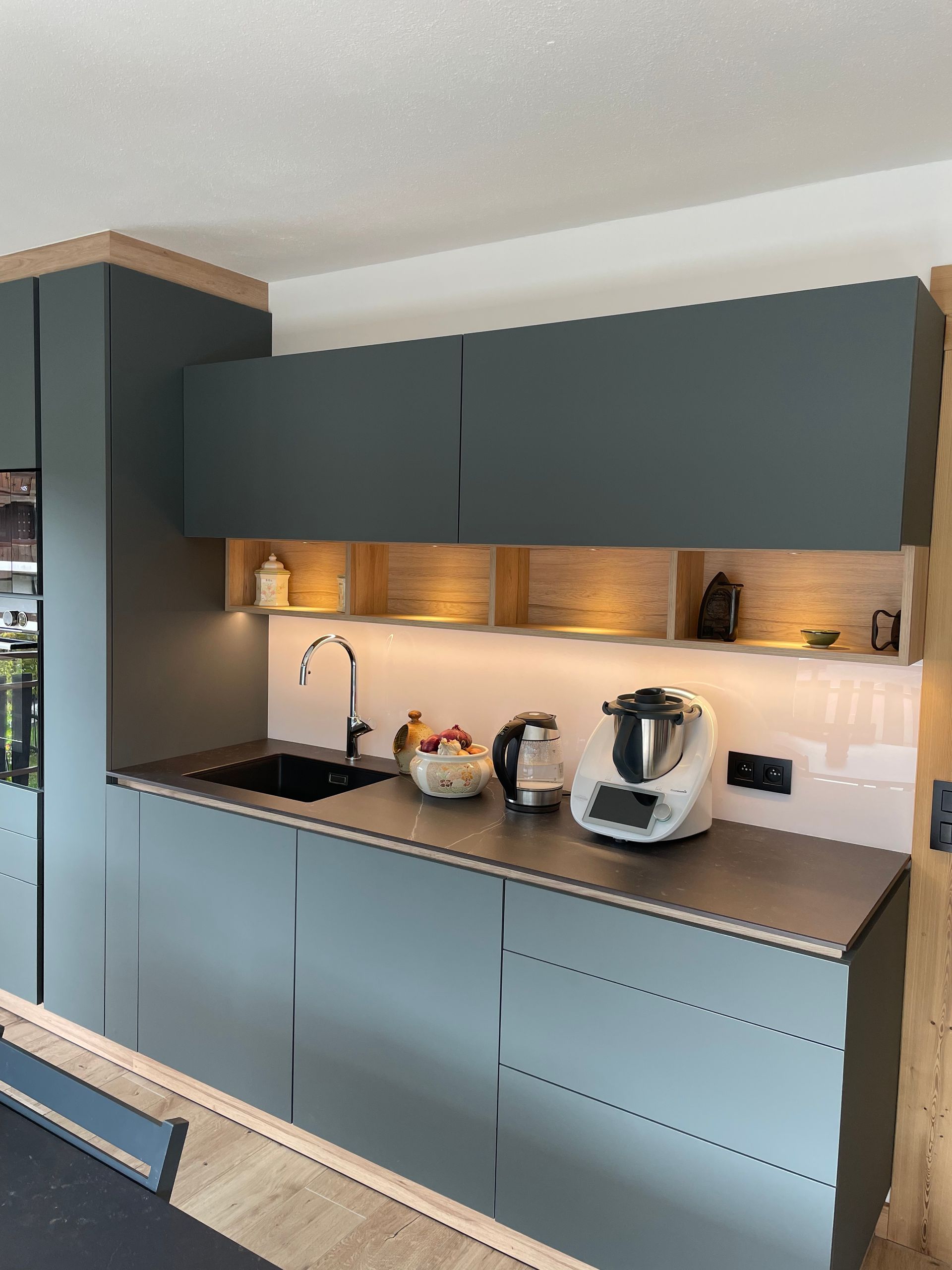 Cuisine moderne avec placards gris, plan de travail noir et touches de bois chaleureux.