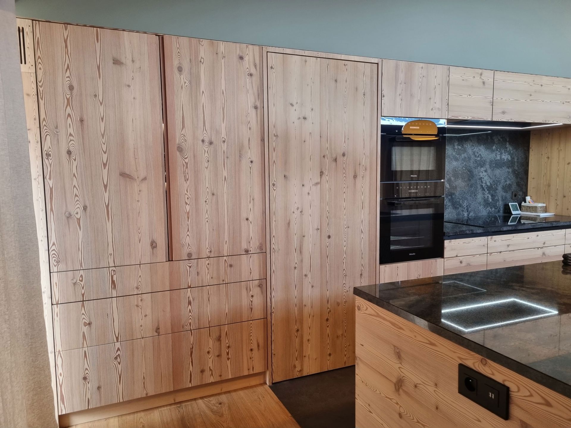 Cuisine équipée d'armoires en bois, d'appareils électroménagers intégrés et d'un plan de travail foncé.