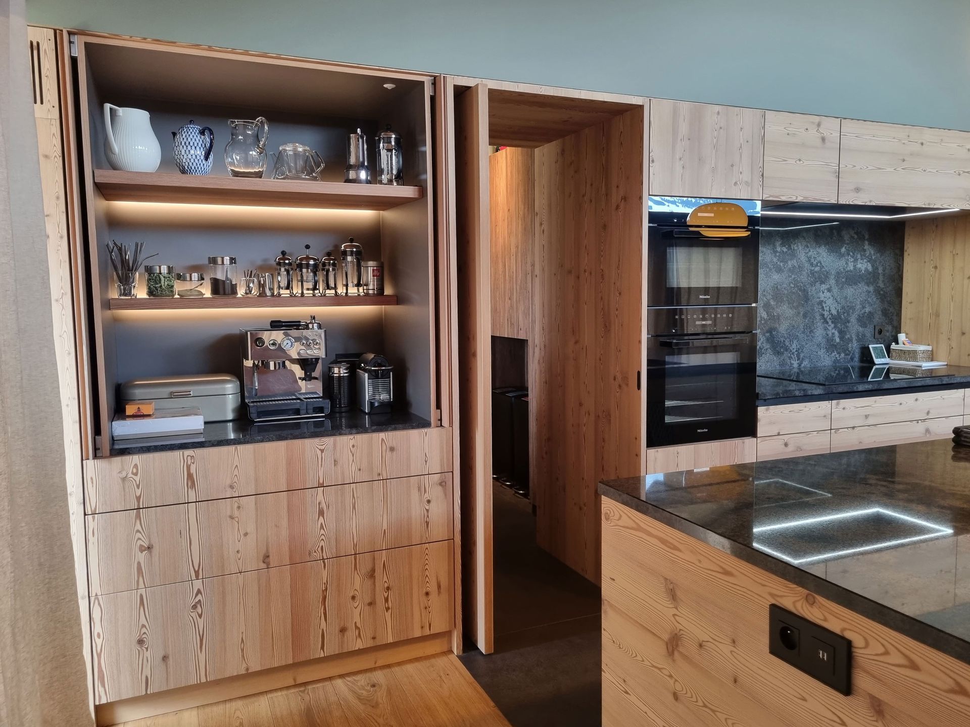 Cuisine avec placards en bois, étagères garnies et appareils électroménagers intégrés.