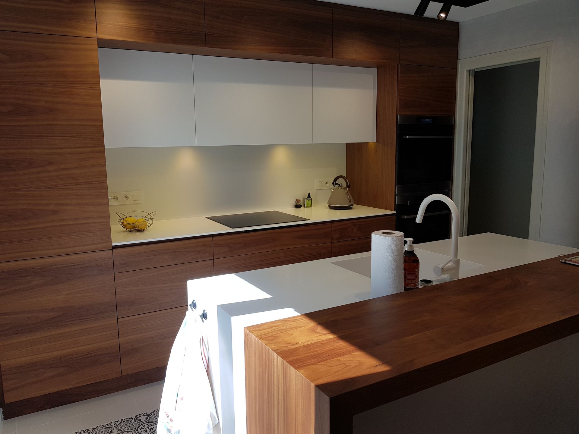 Cuisine moderne avec comptoirs blancs, armoires en bois et îlot central avec évier.