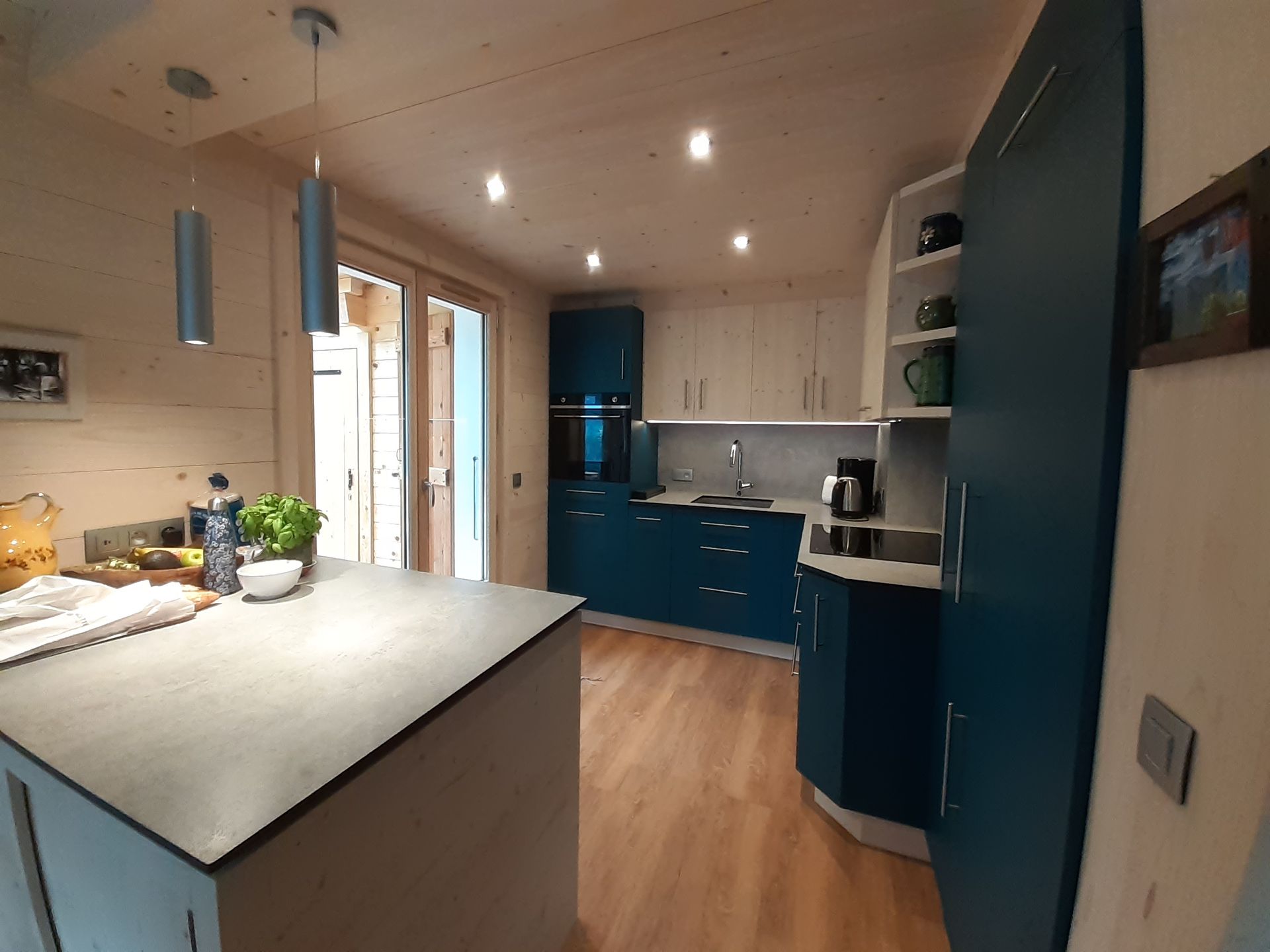 Cuisine moderne avec placards bleu sarcelle, murs en bois clair et îlot gris.