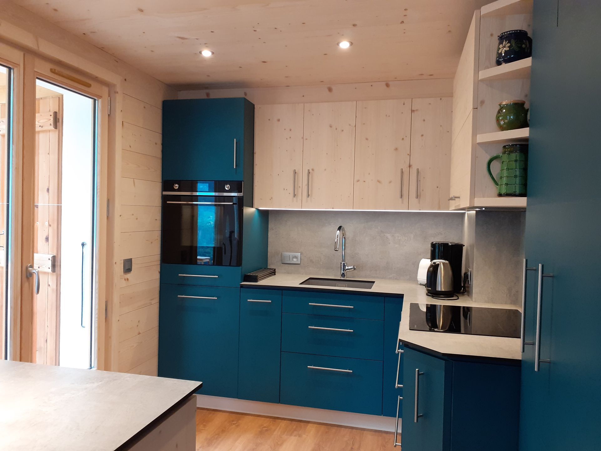 Cuisine turquoise et blanche avec four, évier, placards et étagères ouvertes.