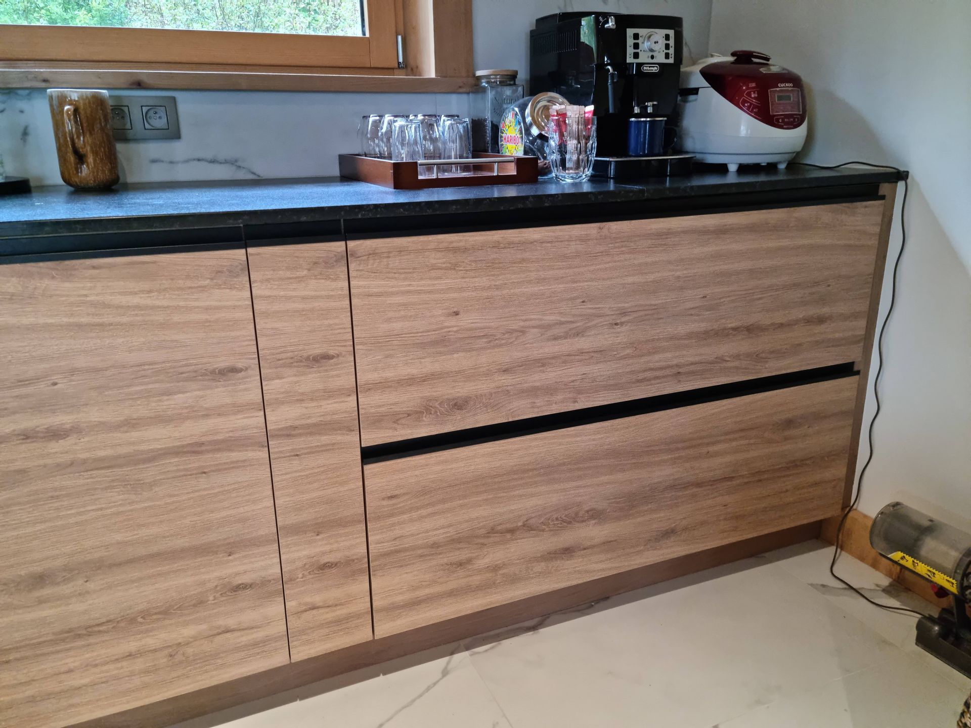 Placards de cuisine en bois sous un plan de travail avec appareils électroménagers et un plateau de verres.