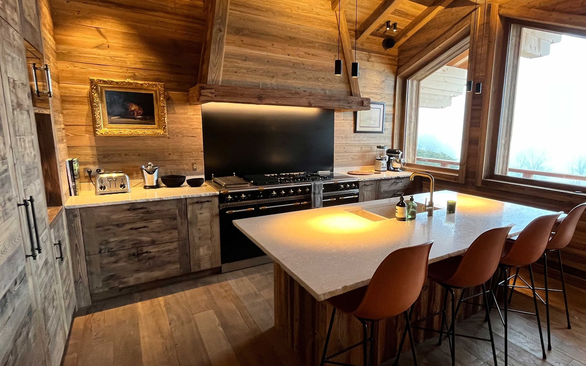 Cuisine rustique en bois avec îlot central et tabourets de bar, cuisinière et tableau encadré.