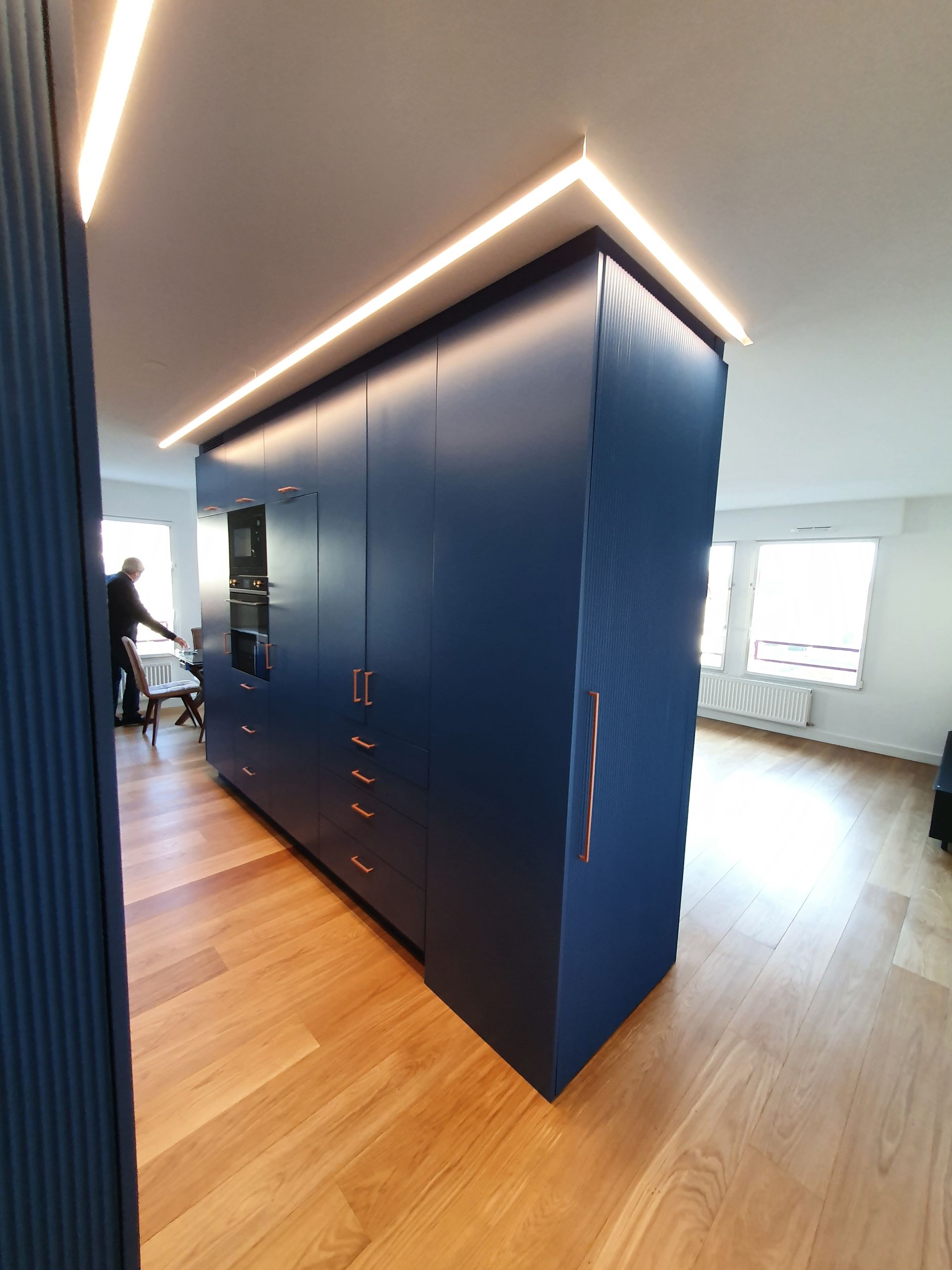 Meubles encastrés bleus avec tiroirs et portes, éclairés par des tubes fluorescents, installés dans une pièce avec parquet.