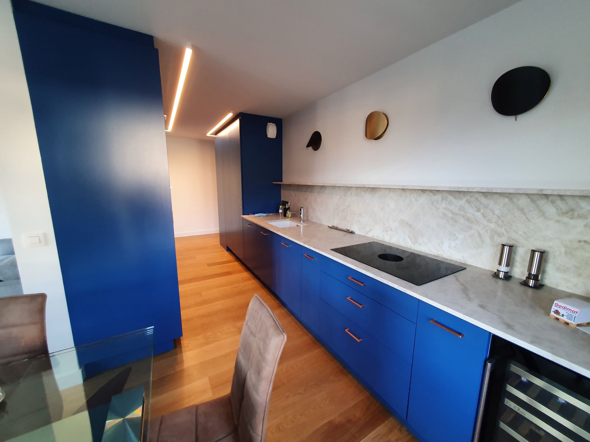 Cuisine bleue moderne avec parquet, crédence en marbre et électroménager intégré.