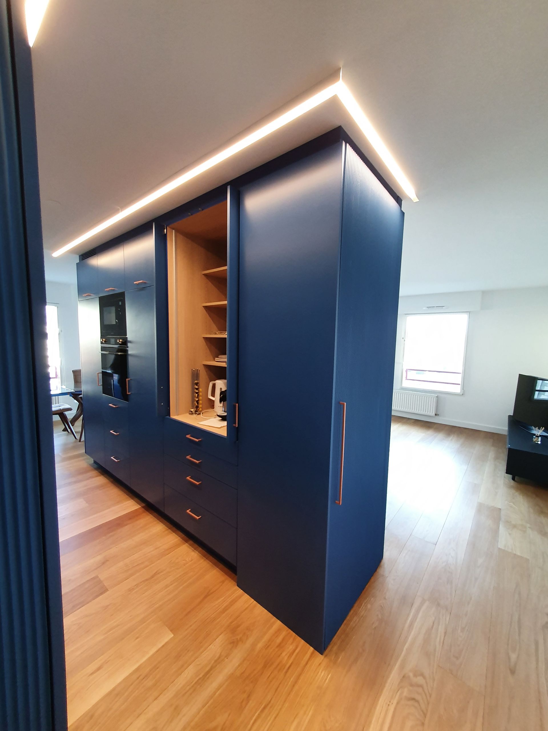 Îlot de cuisine bleu avec placards, tiroirs et garde-manger ouvert avec étagères en bois.