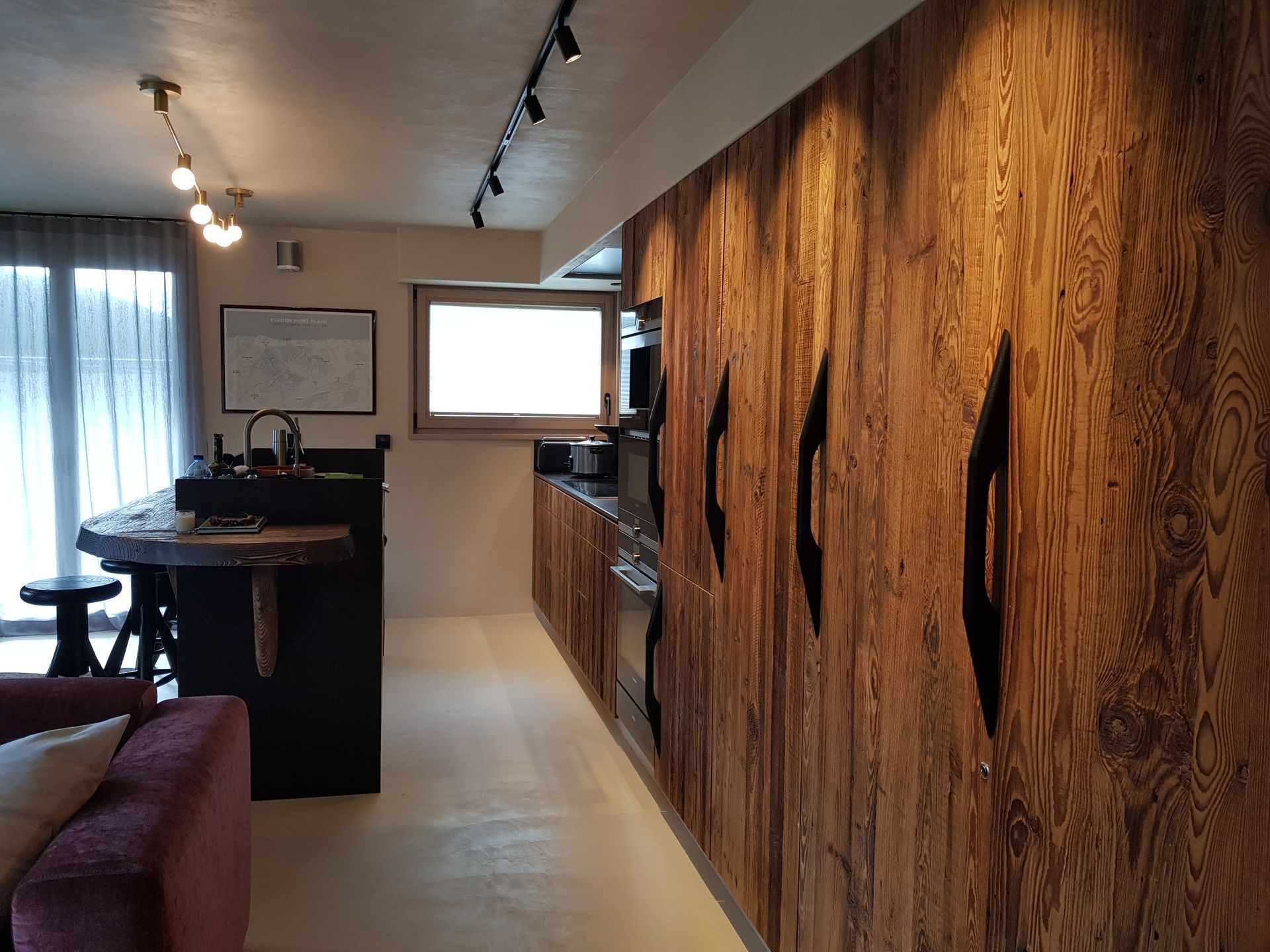 Cuisine moderne avec panneaux de bois et îlot central, éclairage par fenêtre et sur rail.