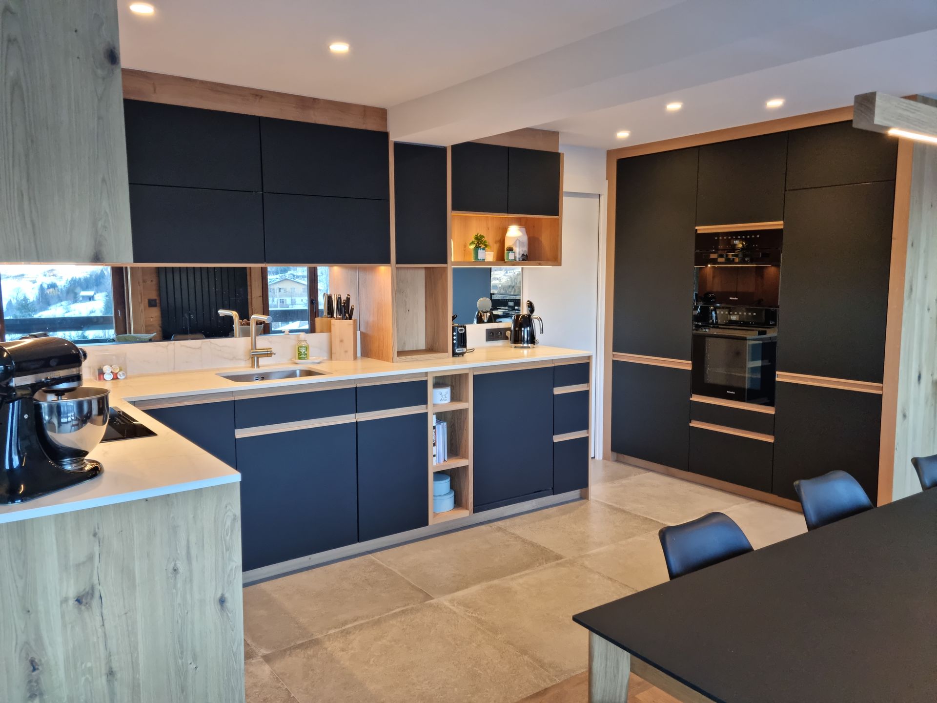 Cuisine moderne avec armoires noires, accents en bois clair et four intégré.