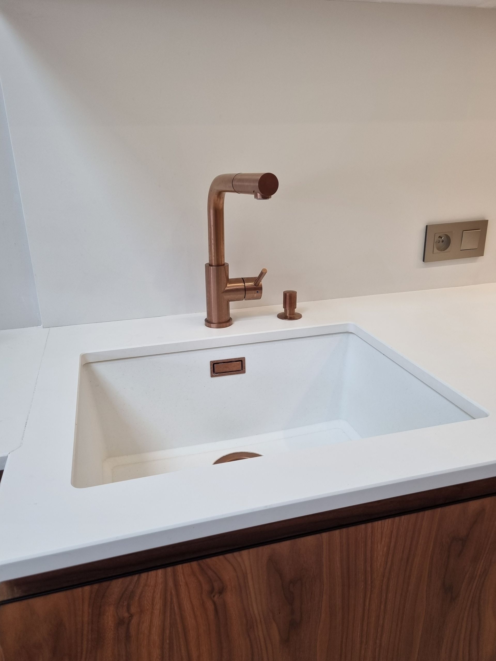 Robinet en cuivre au-dessus d'un évier blanc dans une cuisine moderne avec une base d'armoire en bois et un comptoir blanc.