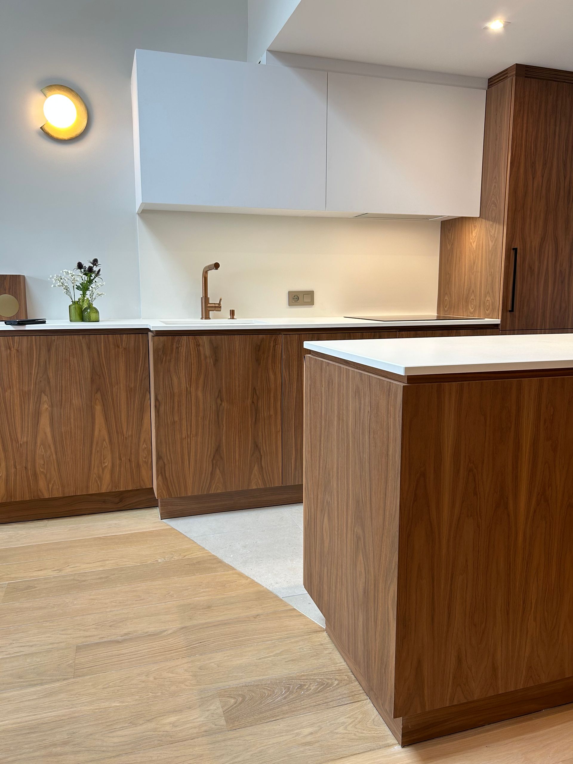 Cuisine moderne avec armoires en bois, comptoirs blancs et éclairage chaleureux.