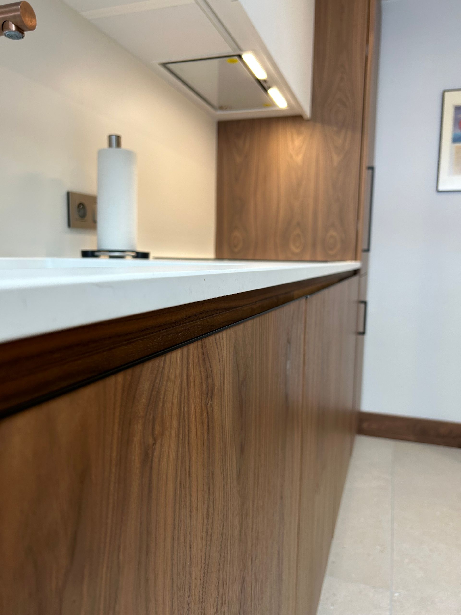 Armoires de cuisine en bois avec plan de travail blanc et éclairage intégré. Un distributeur d'essuie-tout est visible.