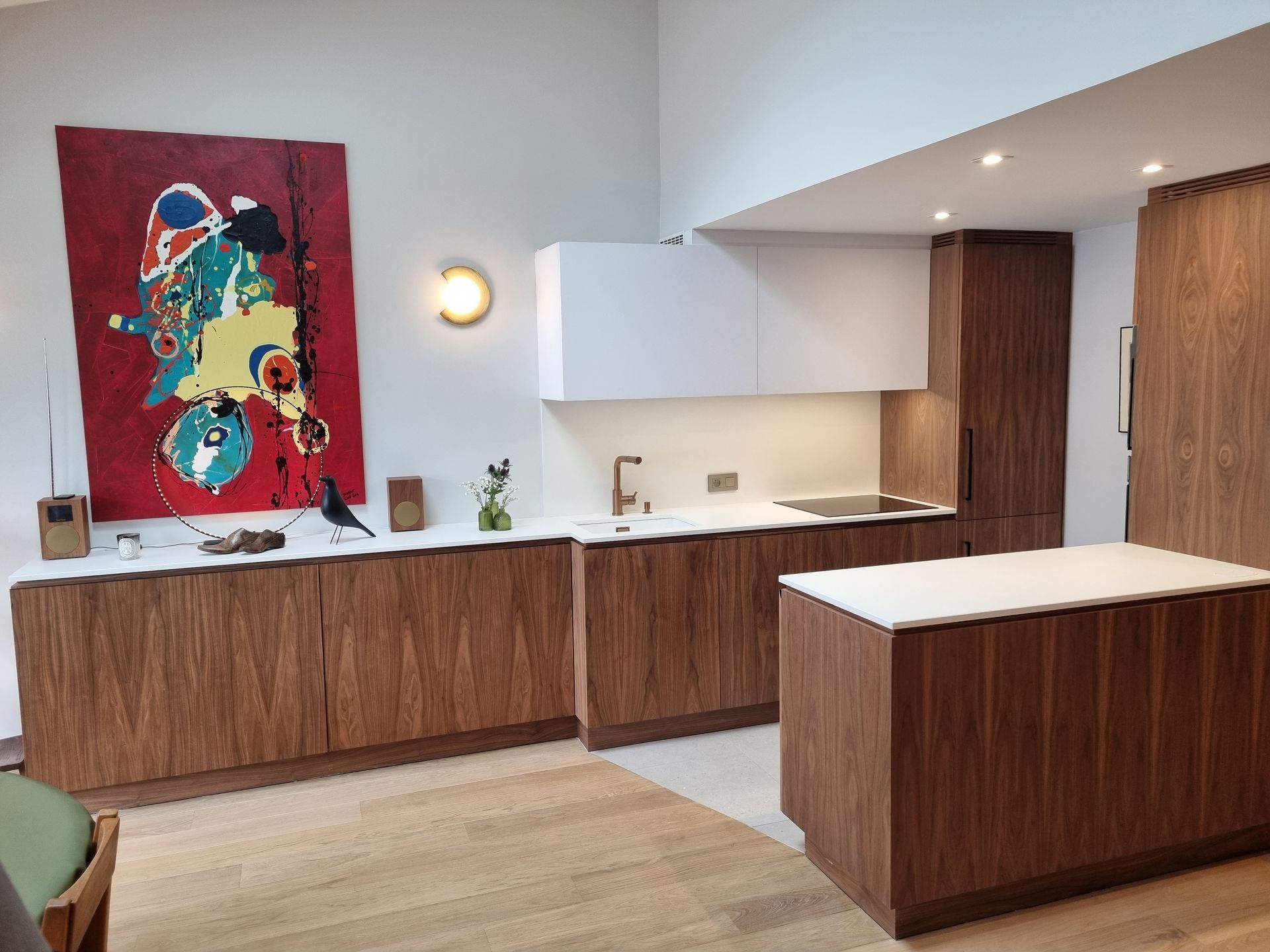 Cuisine moderne avec armoires en noyer, comptoirs blancs, îlot et tableau abstrait rouge.