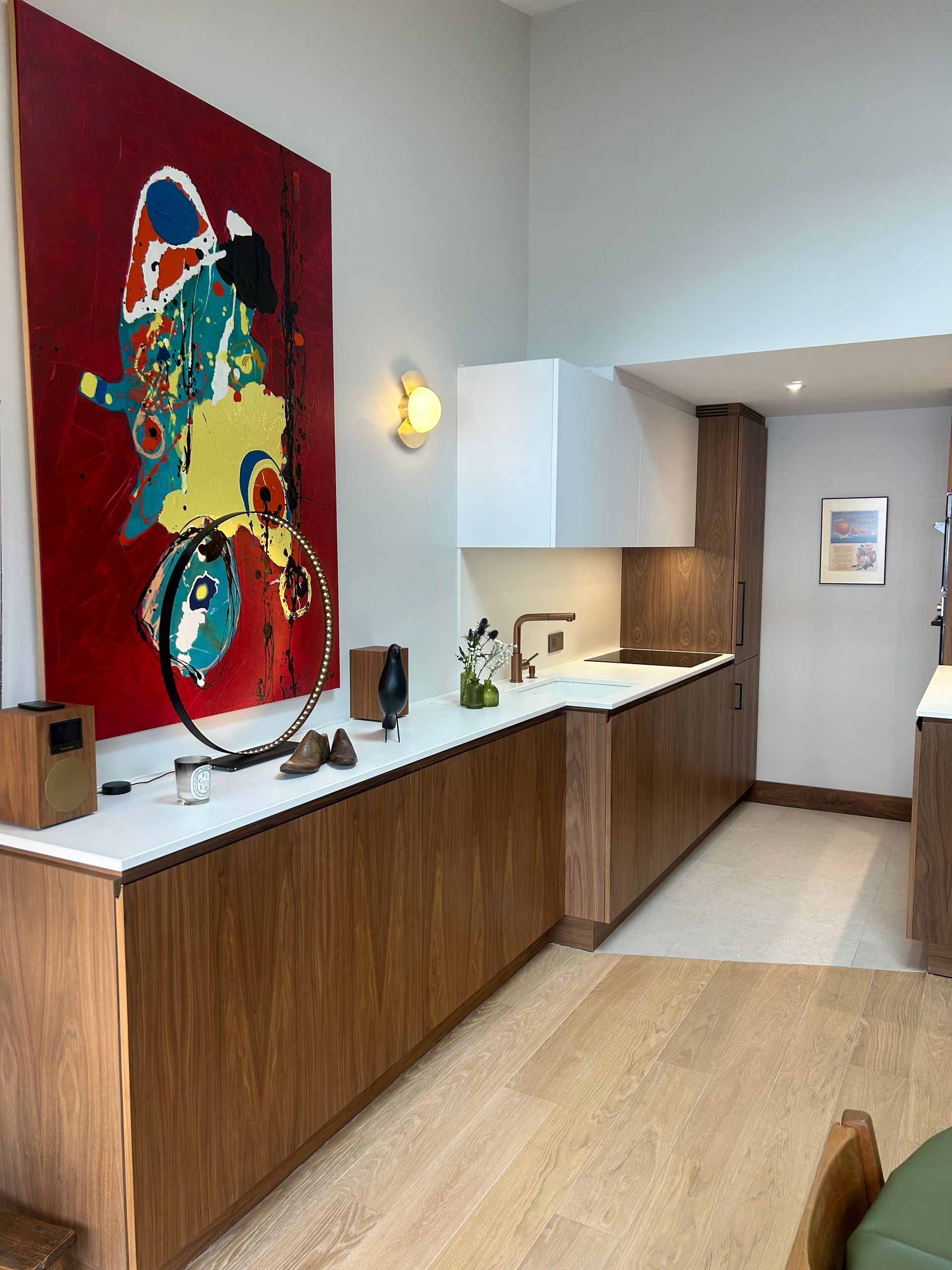 Cuisine moderne avec armoires en bois, comptoirs blancs et œuvres d'art abstraites rouges.