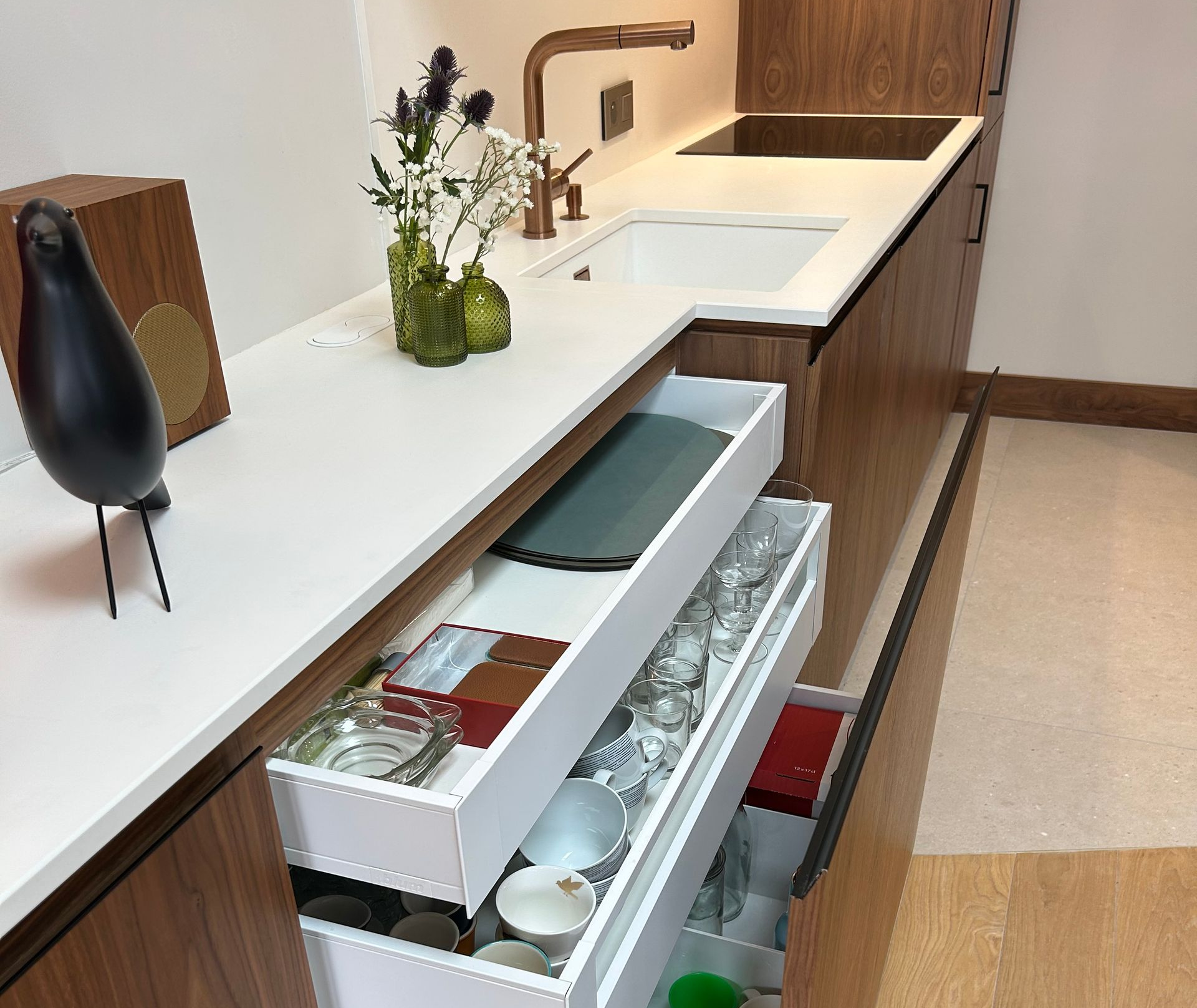 Cuisine moderne avec tiroirs ouverts affichant la vaisselle et les fournitures, comptoir blanc et armoires en bois.