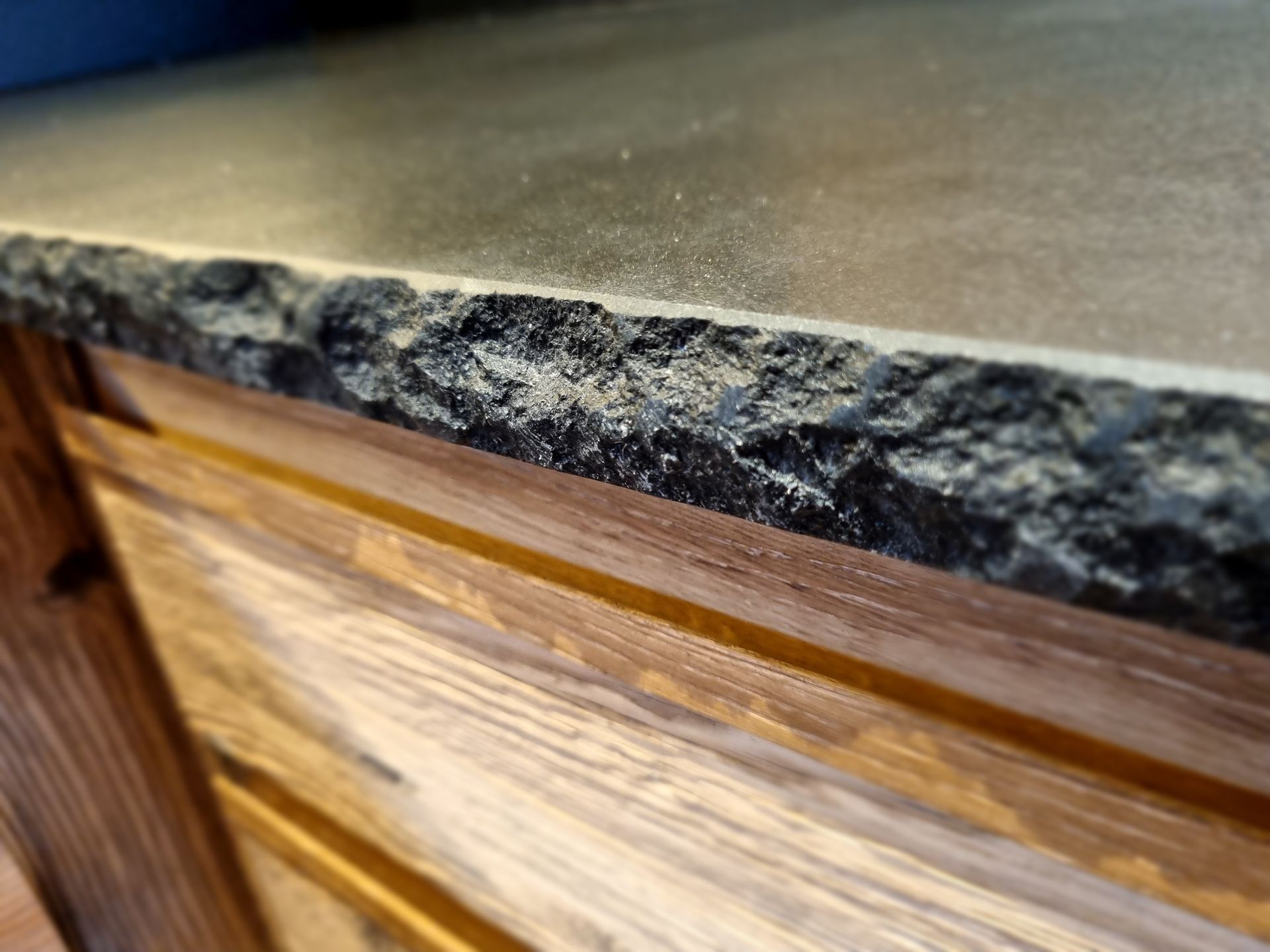 Bord de comptoir en granit à texture rugueuse, au-dessus d'un meuble en bois à tiroirs horizontaux.