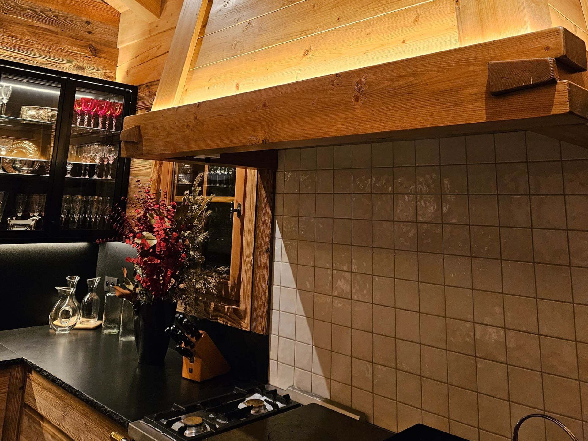 Hotte de cuisine en bois avec éclairage chaleureux, au-dessus d'une plaque de cuisson avec crédence en carrelage blanc.