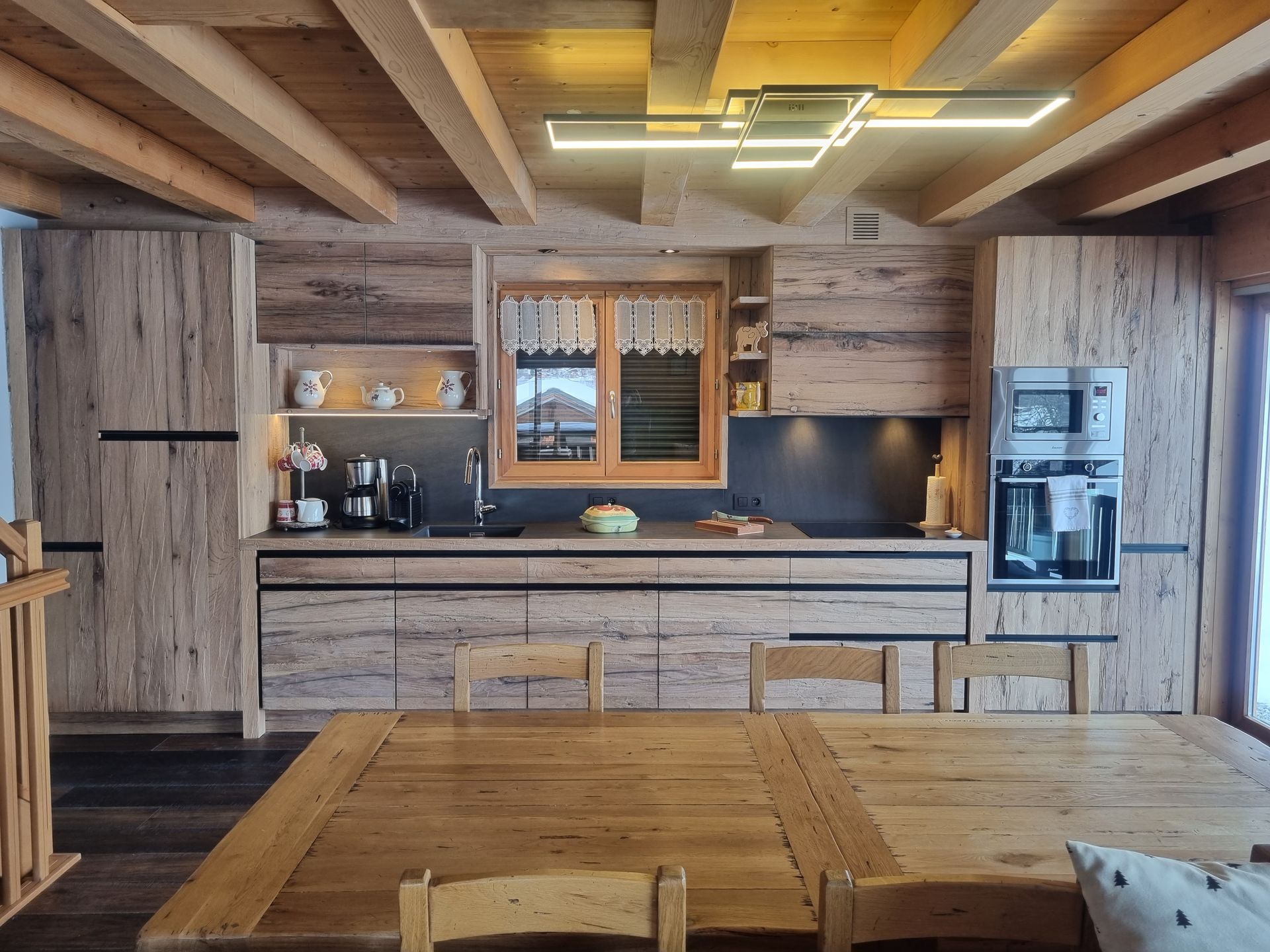 Cuisine rustique en bois avec éclairage zénithal, placards et une table centrale avec chaises.