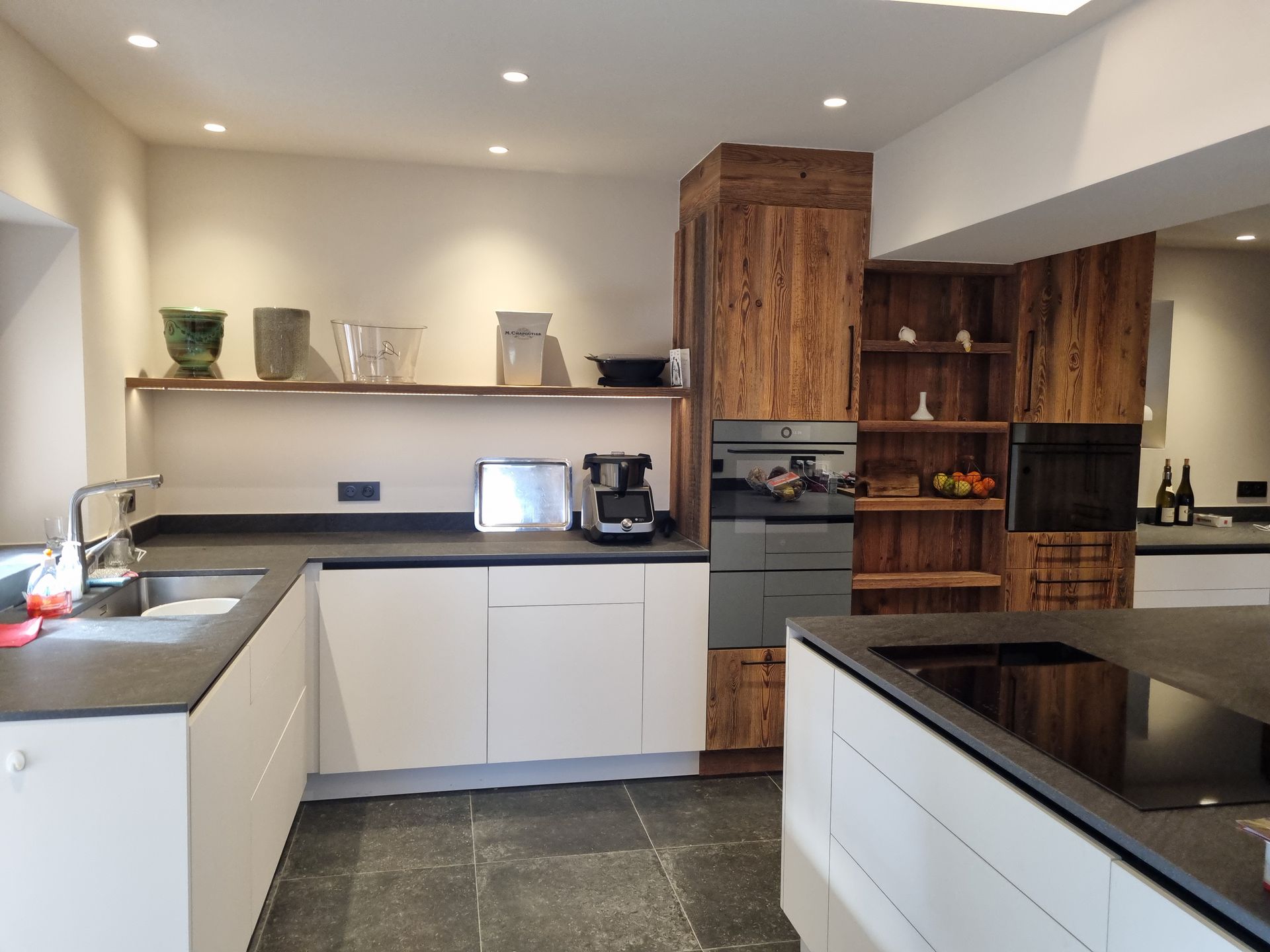 Cuisine moderne avec armoires blanches, comptoirs foncés et éléments en bois.