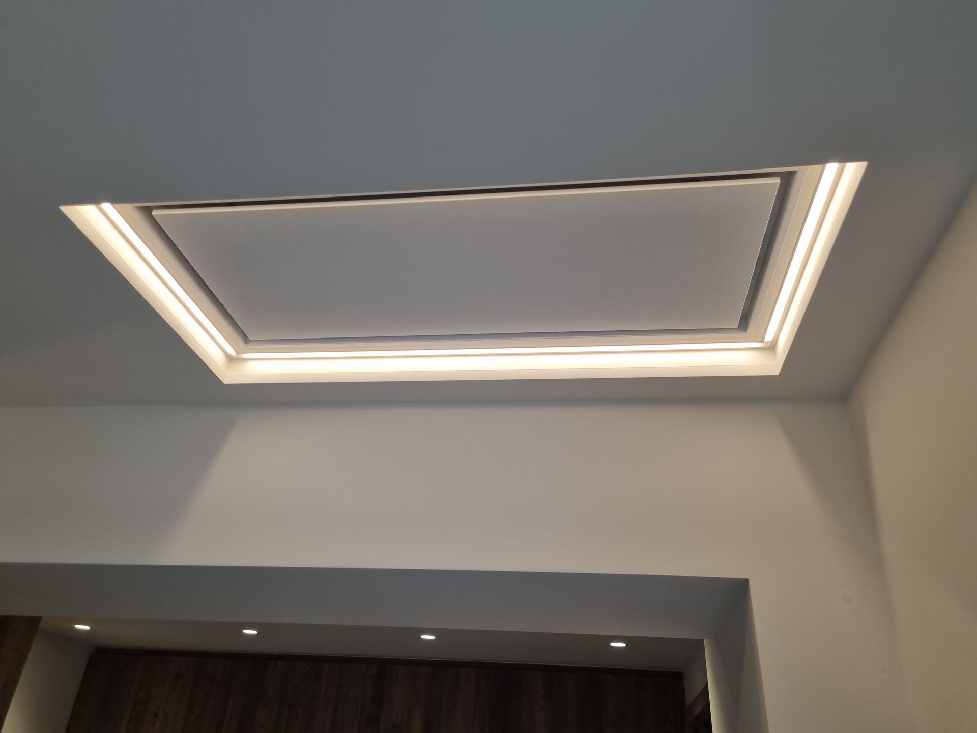 Plafond encastré avec luminaire rectangulaire. Murs blancs, lumière chaude.