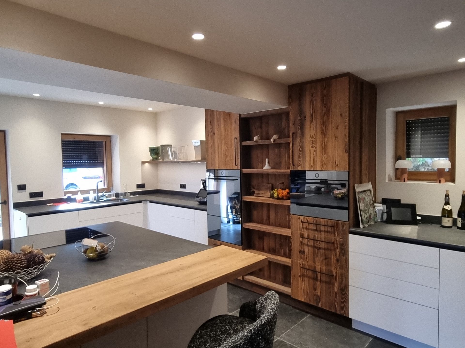 Cuisine moderne avec des armoires en bois et blanches, un plan de travail foncé et un îlot central avec un plan de travail en bois.