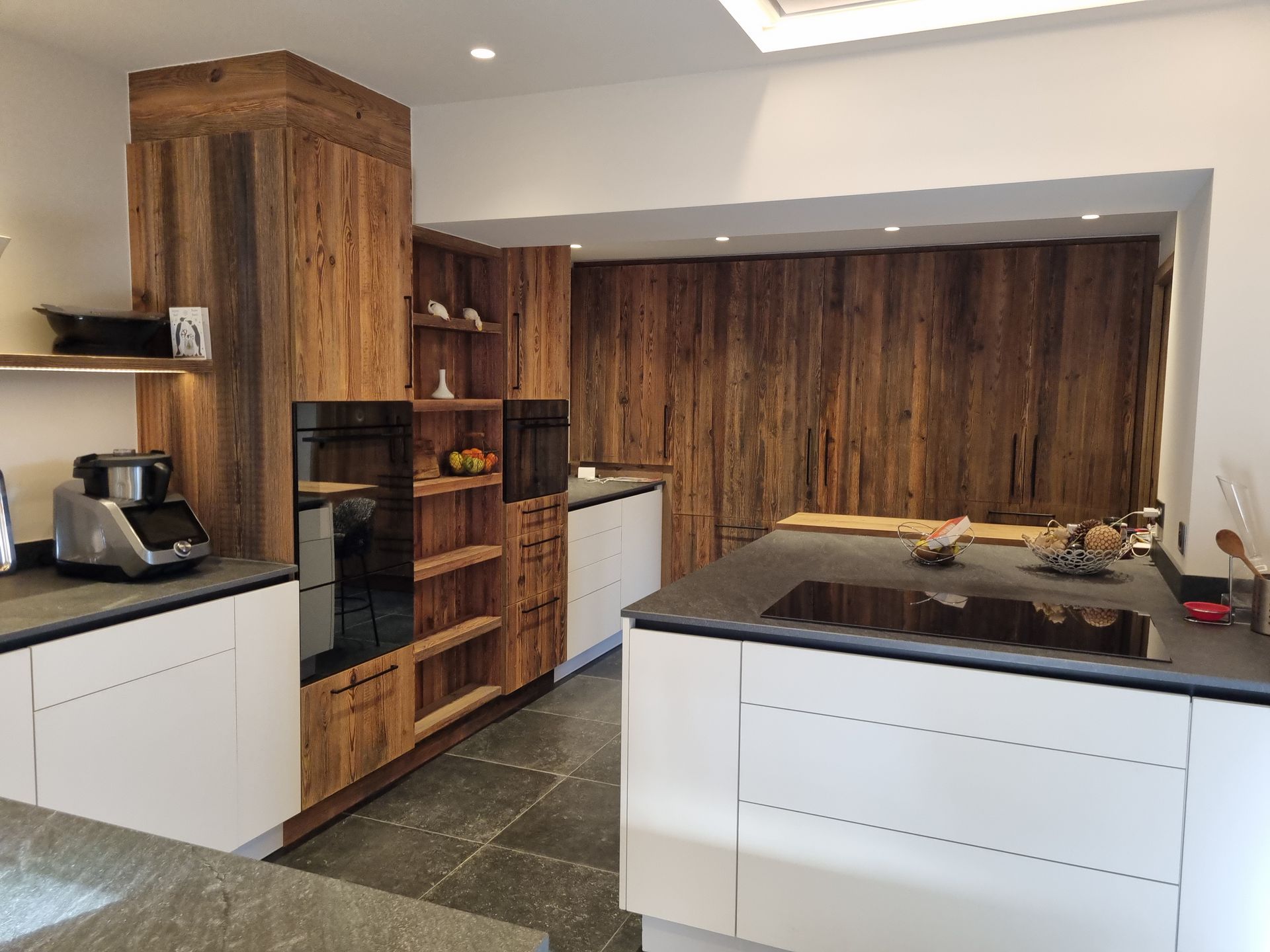 Cuisine moderne avec armoires blanches, lambris et îlot central avec comptoir noir.