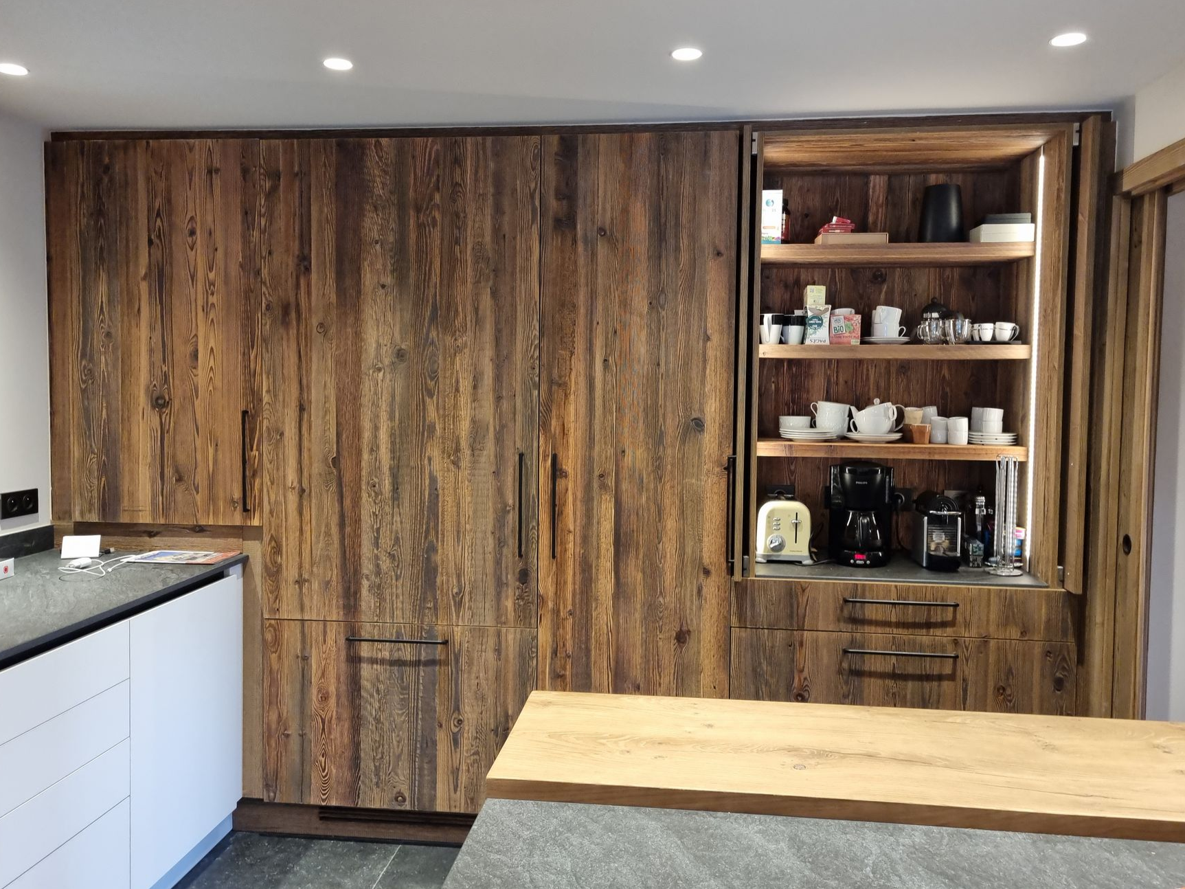 Meubles de cuisine en bois avec une partie ouverte présentant des étagères où sont rangés la vaisselle et les appareils électroménagers.