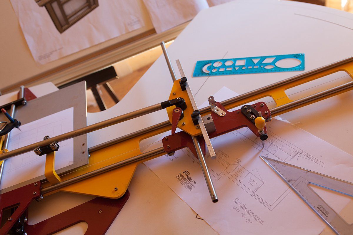 Table à dessin avec règle parallèle et outils de dessin, masquant partiellement les croquis architecturaux.