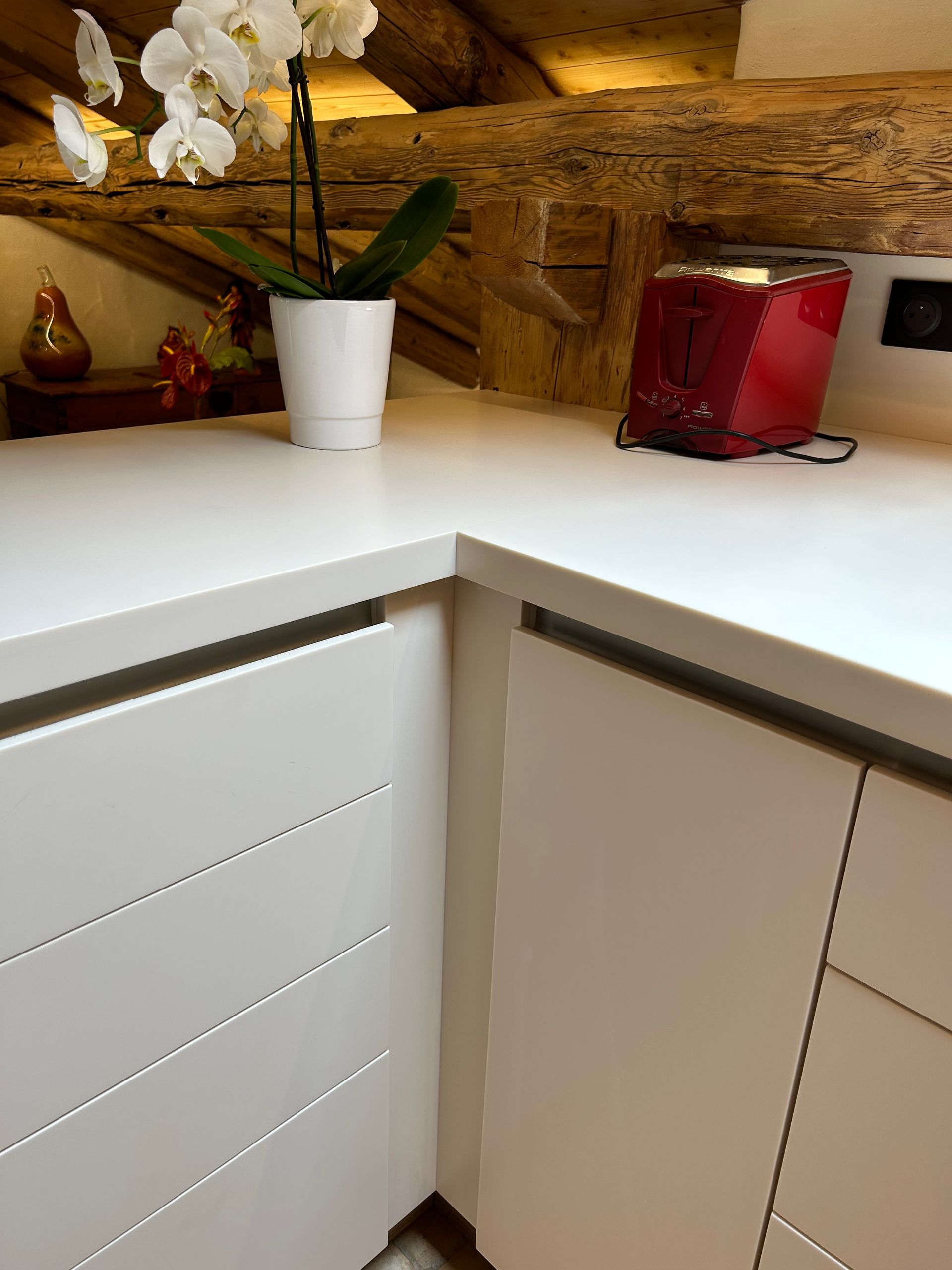 Plan de travail blanc, placards blancs et grille-pain rouge. Une orchidée en pot blanc est posée sur le plan de travail.
