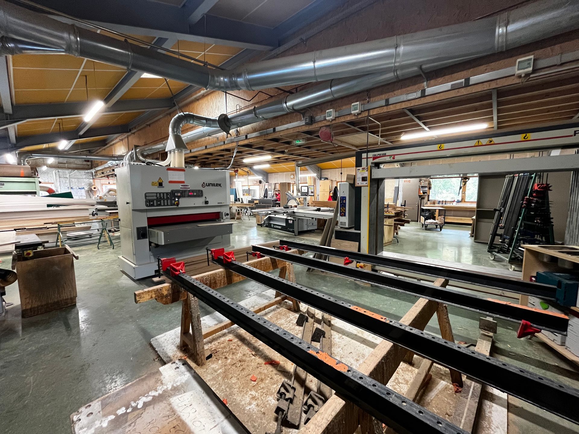 Intérieur d'un atelier avec machines à bois, ventilation par le plafond et une charpente en bois au premier plan.