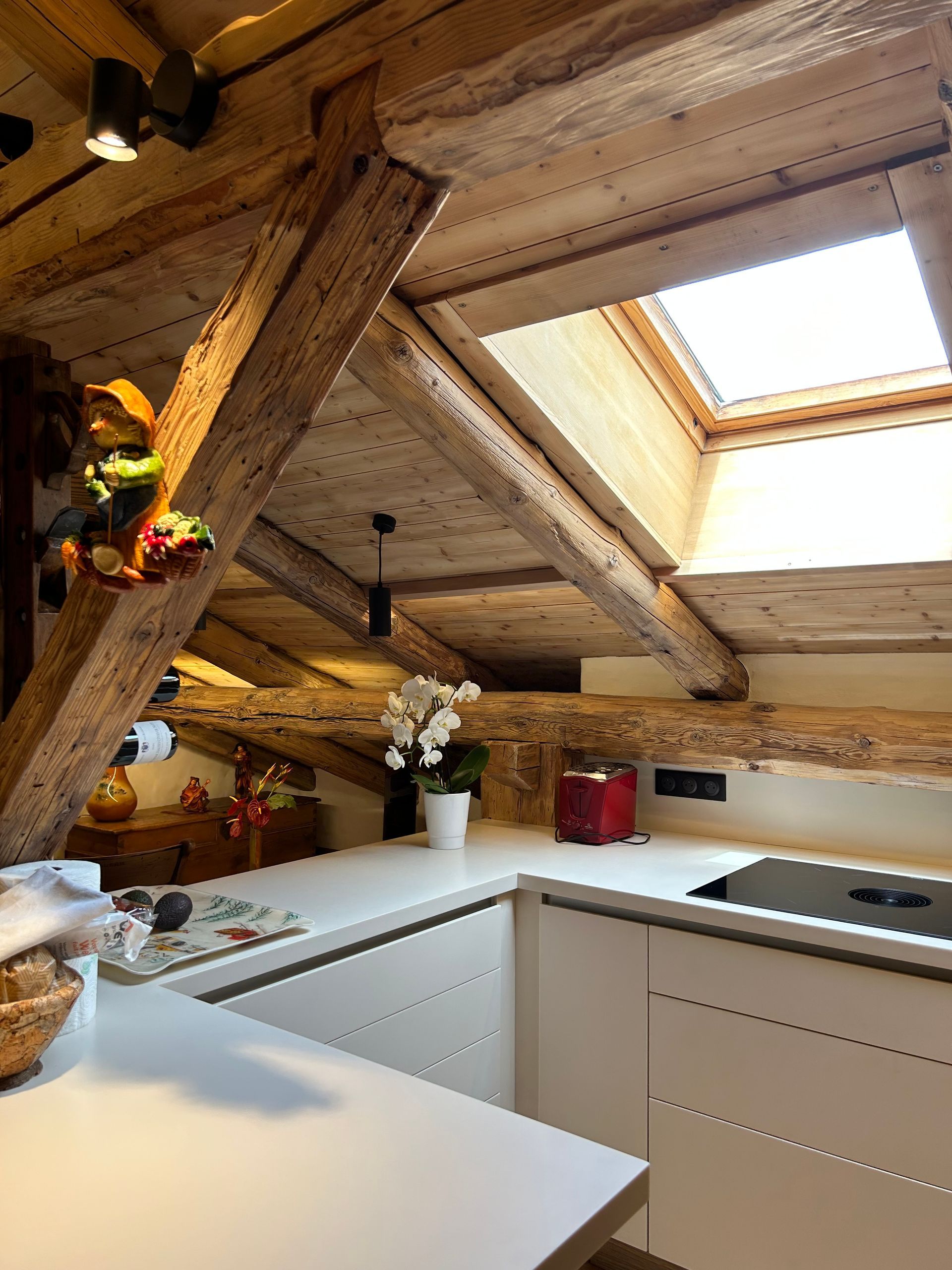 Cuisine avec placards blancs, plans de travail clairs, poutres apparentes et puits de lumière.