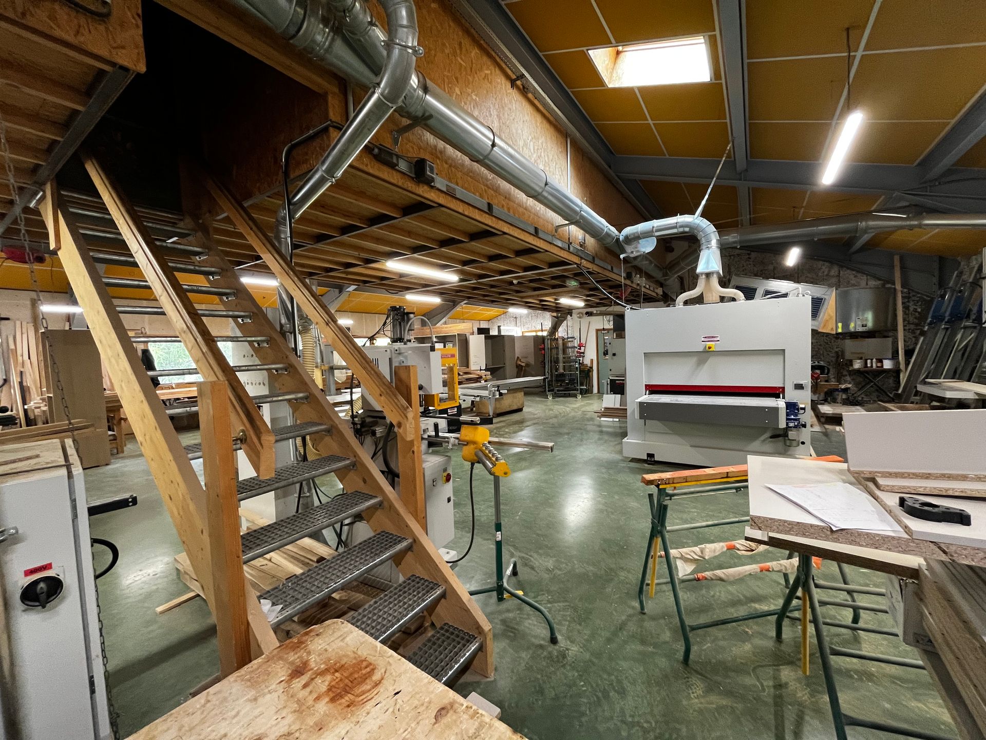 Intérieur d'atelier avec escalier en bois, machines et conduits de ventilation.