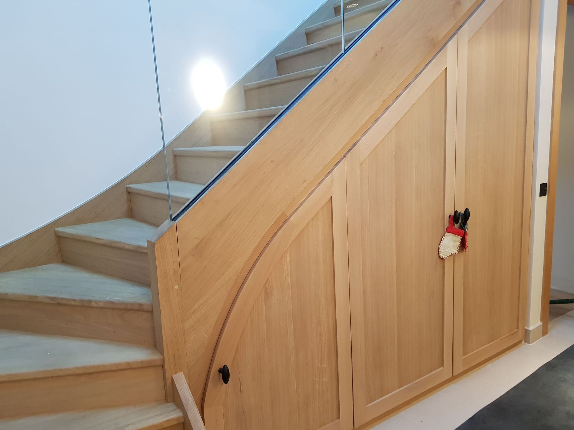 Escalier en bois avec placards de rangement intégrés en dessous, et garde-corps en verre.