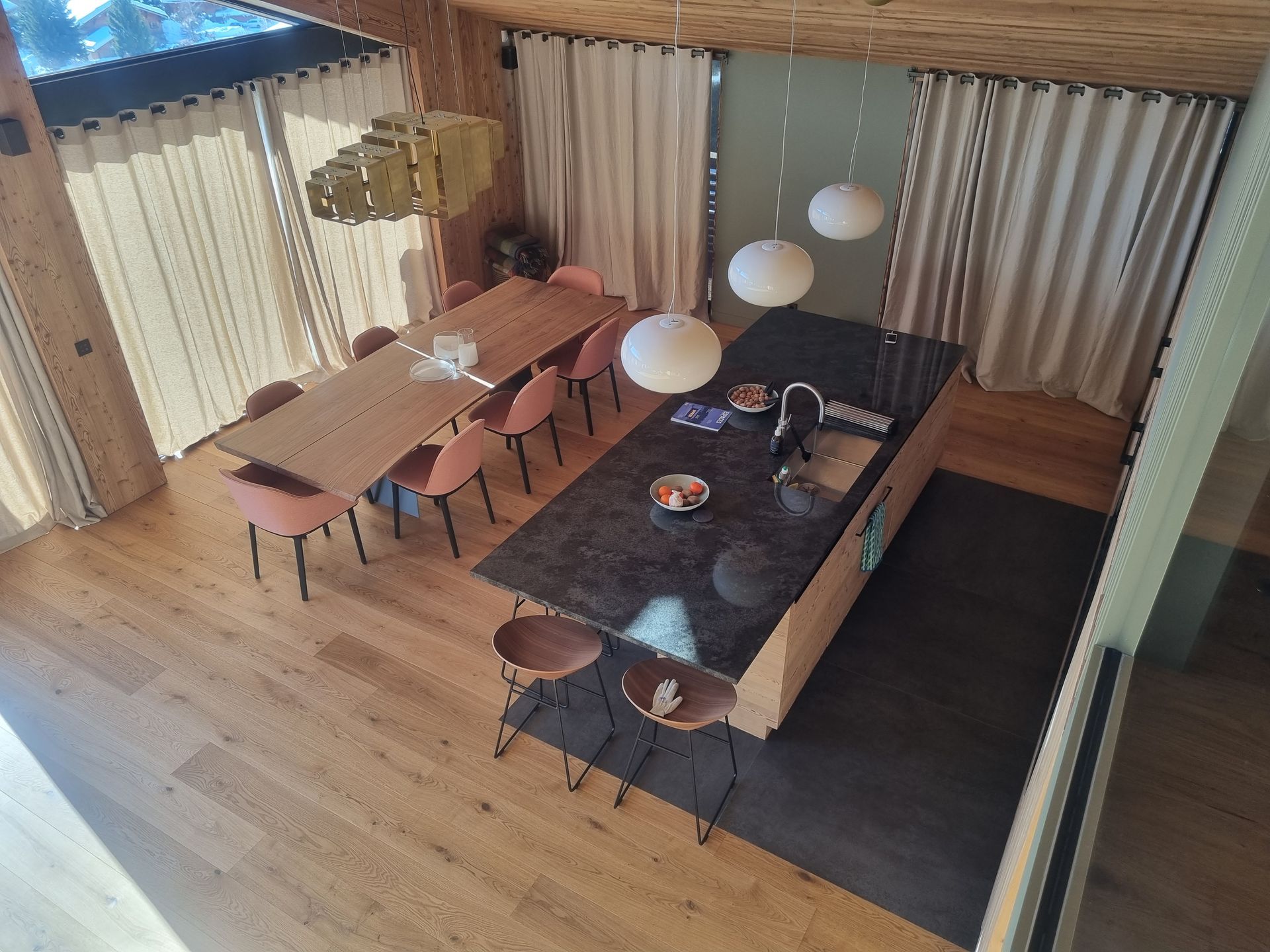 Vue en plongée d'une cuisine moderne avec un grand îlot central, une table à manger et un parquet clair.