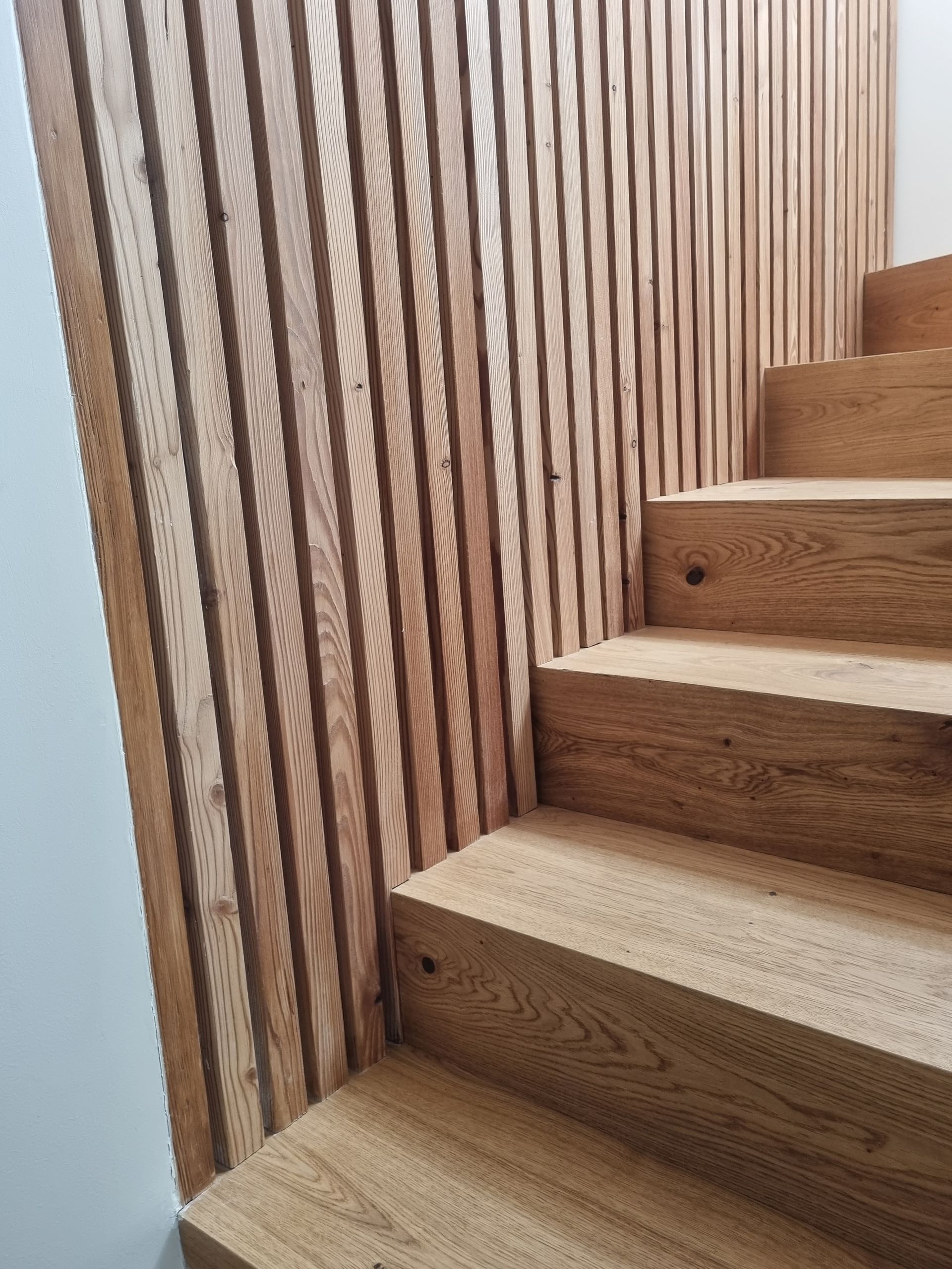 Escalier en bois avec paroi à lattes verticales.
