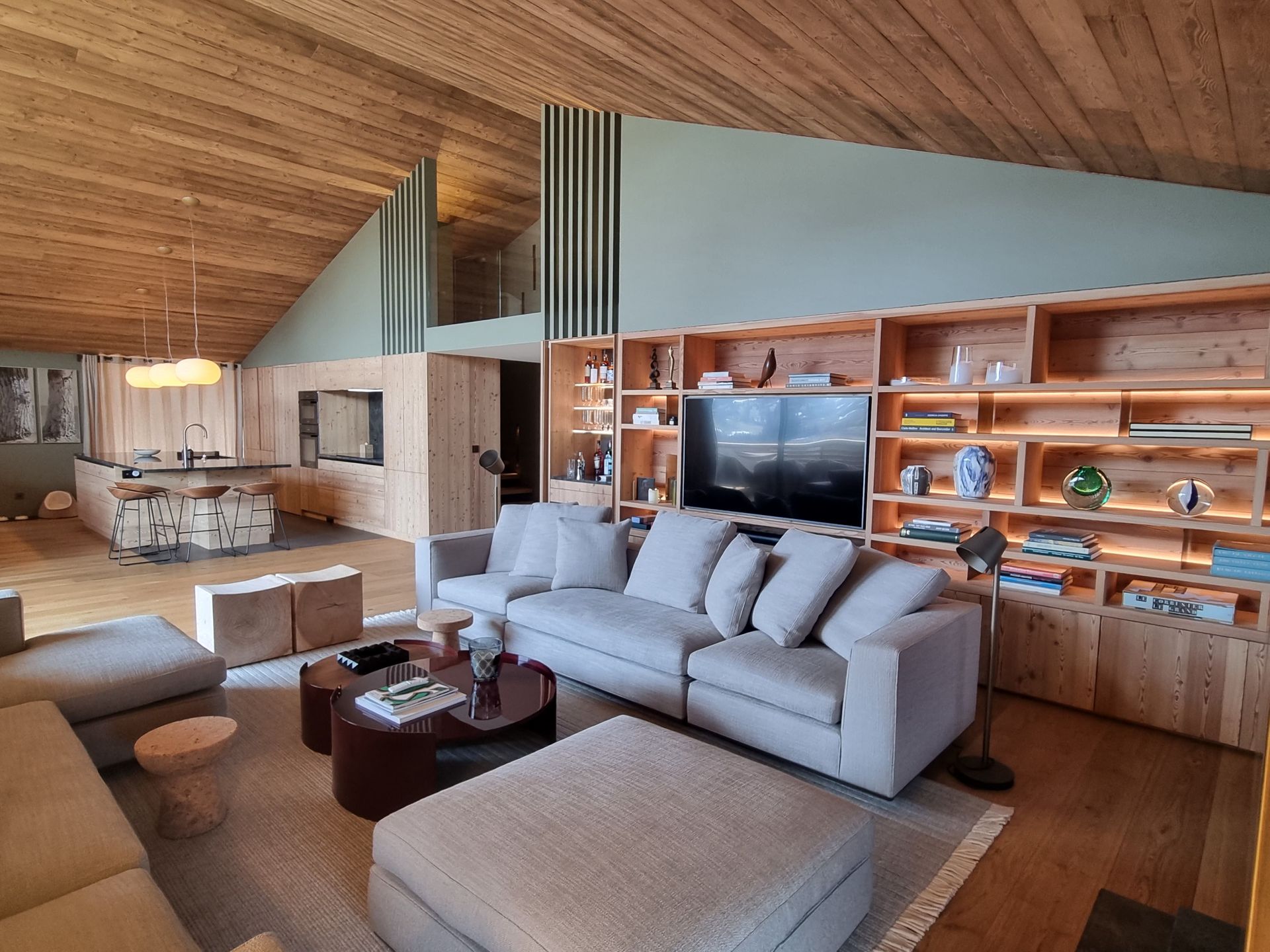 Salon spacieux avec murs et plafond en bois, canapé gris, étagères intégrées, télévision et table basse.
