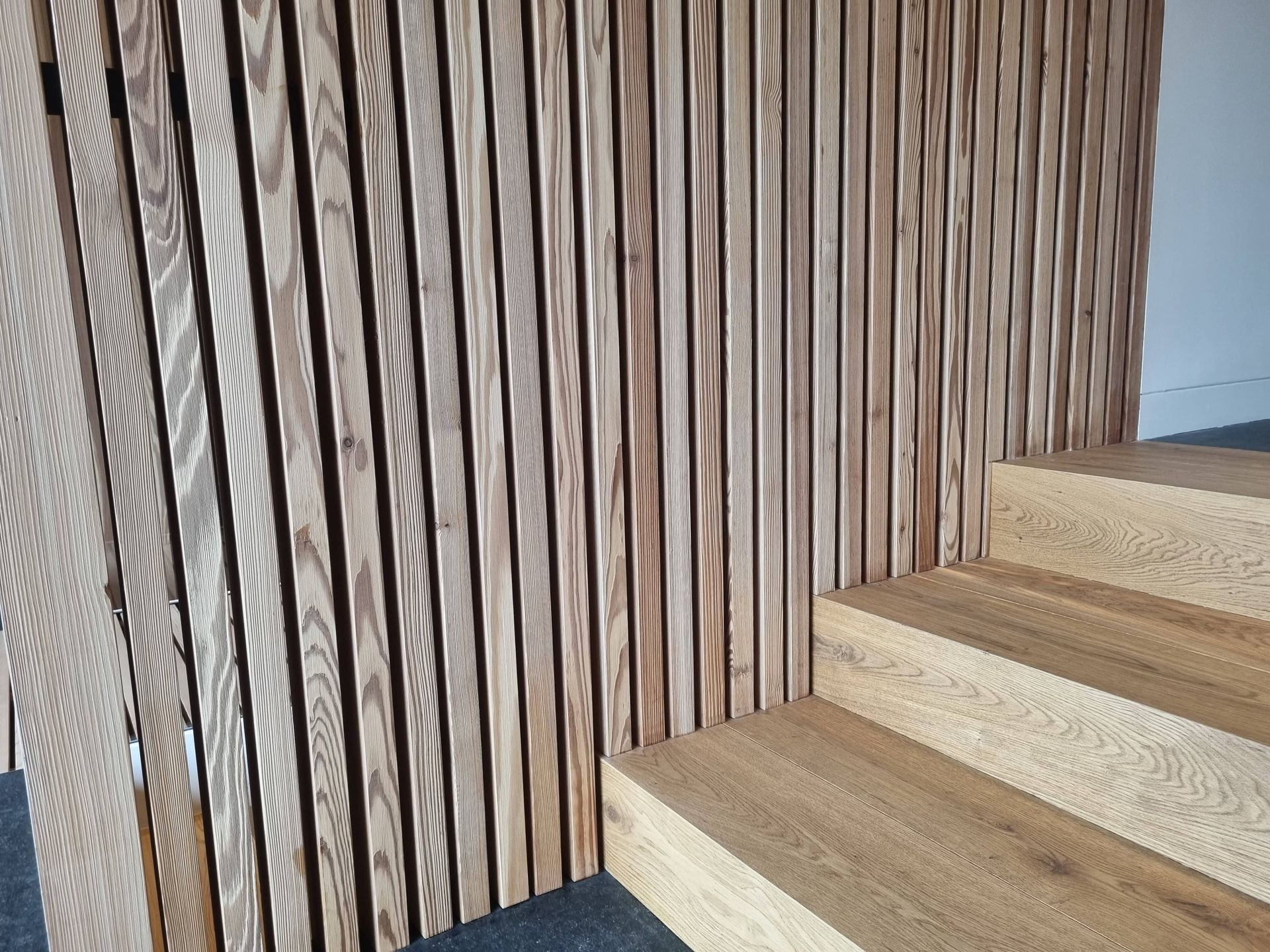 Mur et escalier en lattes de bois brun clair.
