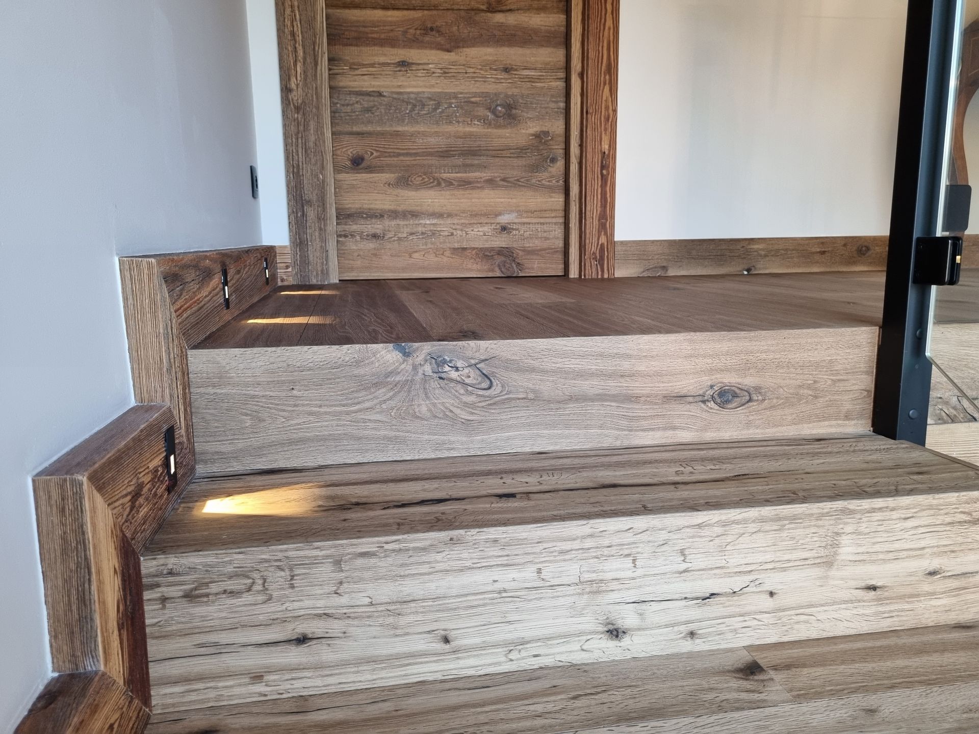 Escalier en bois avec éclairage intégré menant à une porte en bois.