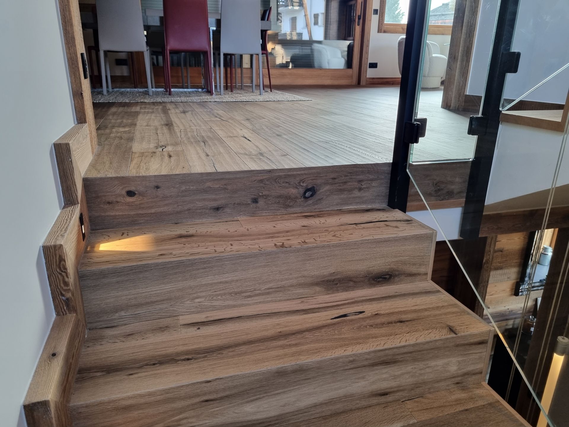 Escalier en bois avec éclairage intégré, rampe en verre et suspensions lumineuses modernes.