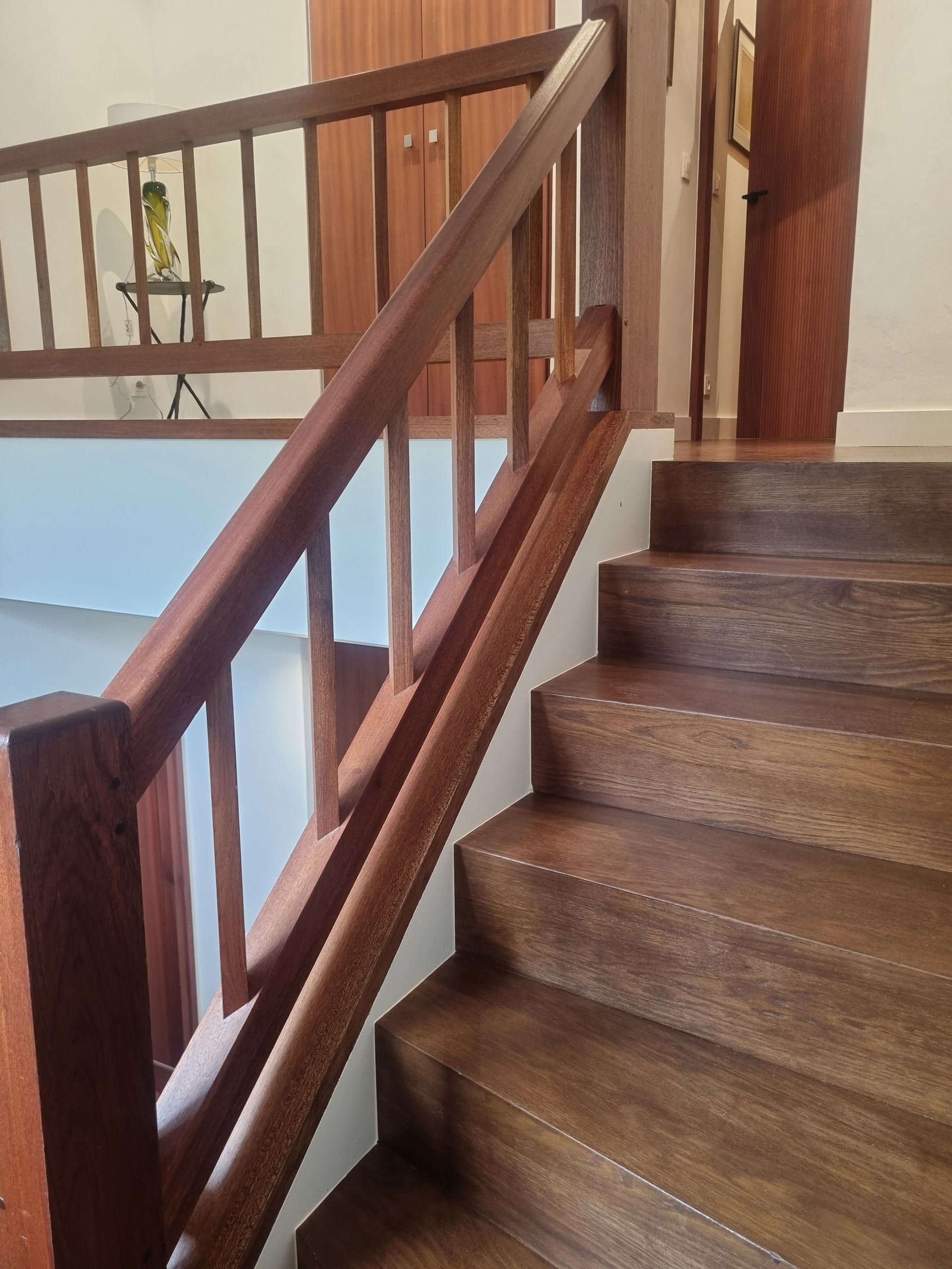 Escalier en bois avec rampe et balustres foncés, adossé à un mur de couleur neutre.