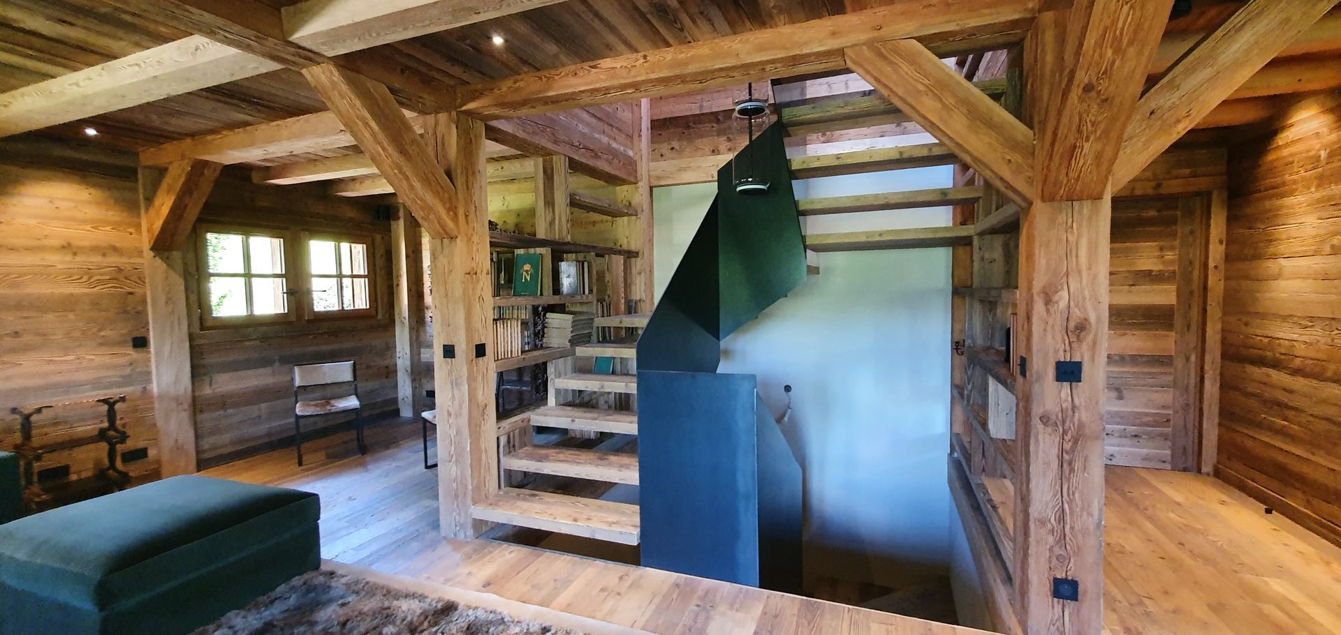 Vue intérieure d'une cabane rustique en bois avec un escalier, des étagères à livres et un canapé vert.