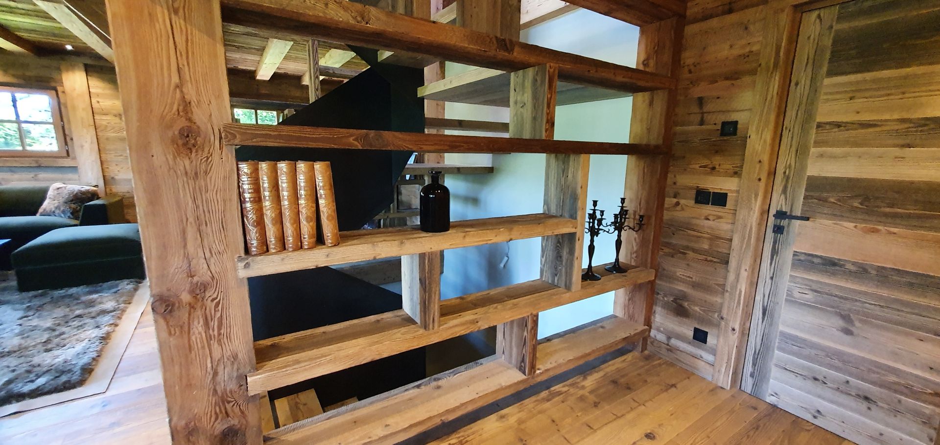 Étagère en bois dans un intérieur rustique, présentant des livres et des bouteilles.