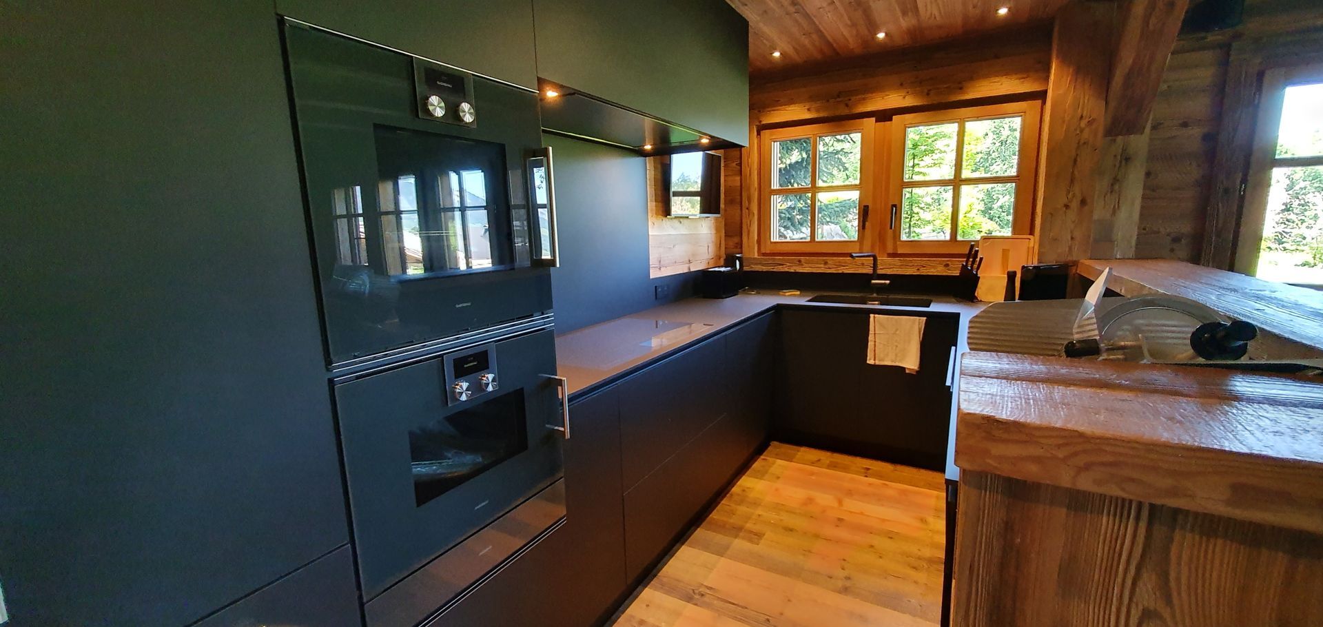 Cuisine moderne avec placards foncés, four encastré, éléments en bois et fenêtre.