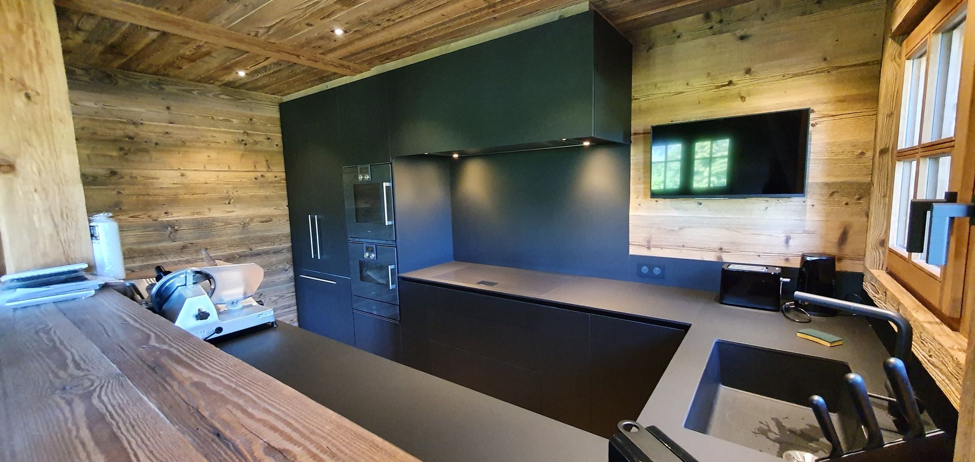 Cuisine avec placards foncés, murs en bois, une télévision et une fenêtre.