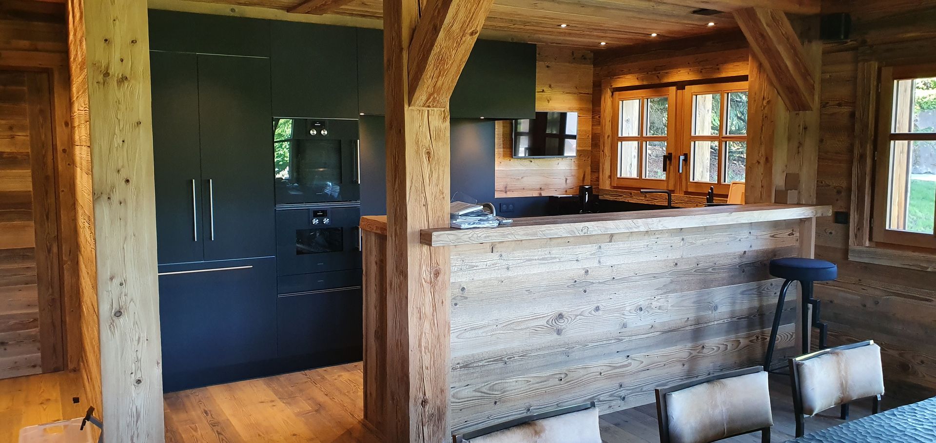 Intérieur rustique avec poutres apparentes, placards de cuisine sombres et un bar avec des places assises.
