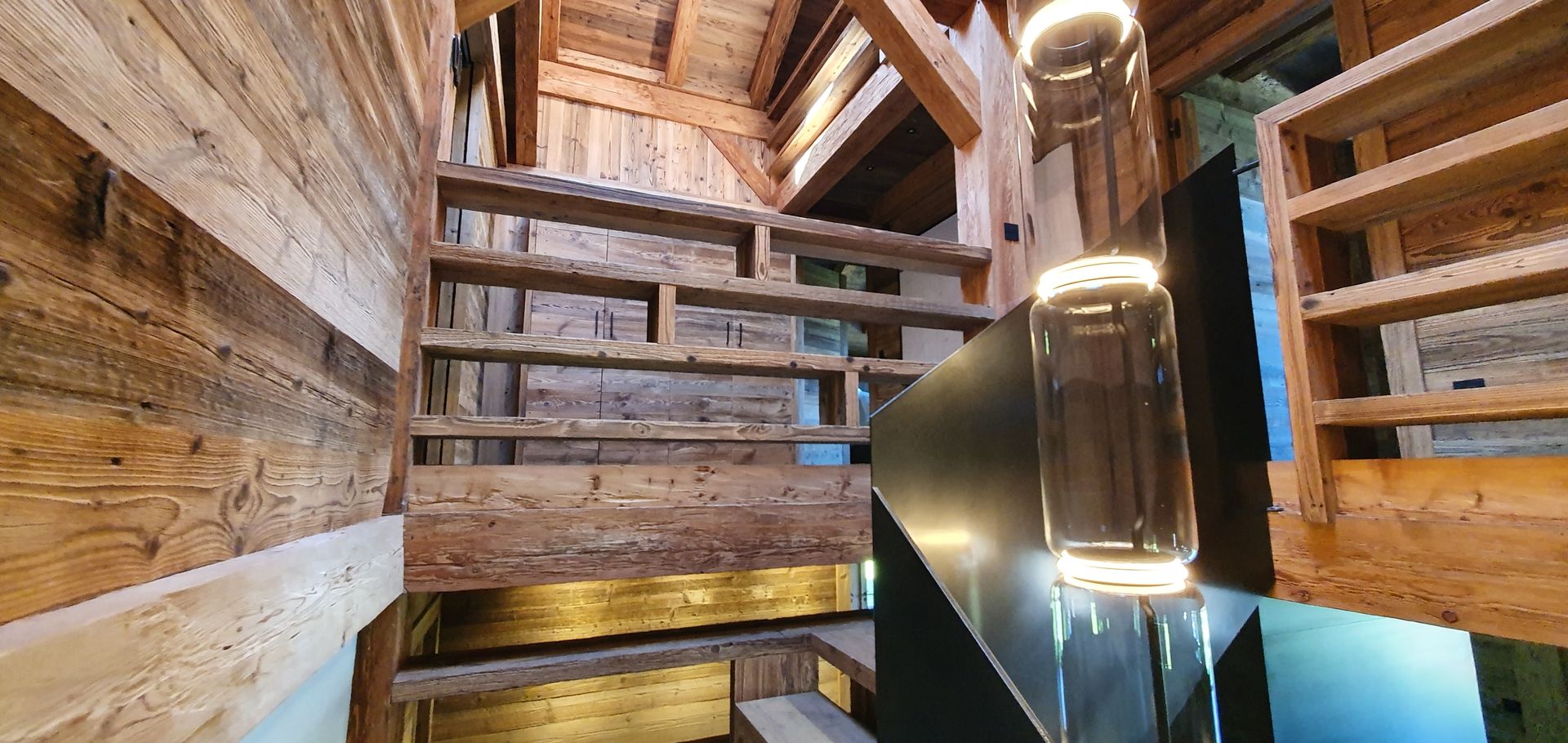 Escalier en bois dans un intérieur avec des marches ressemblant à des étagères, éclairé par un éclairage moderne, avec une charpente en bois.