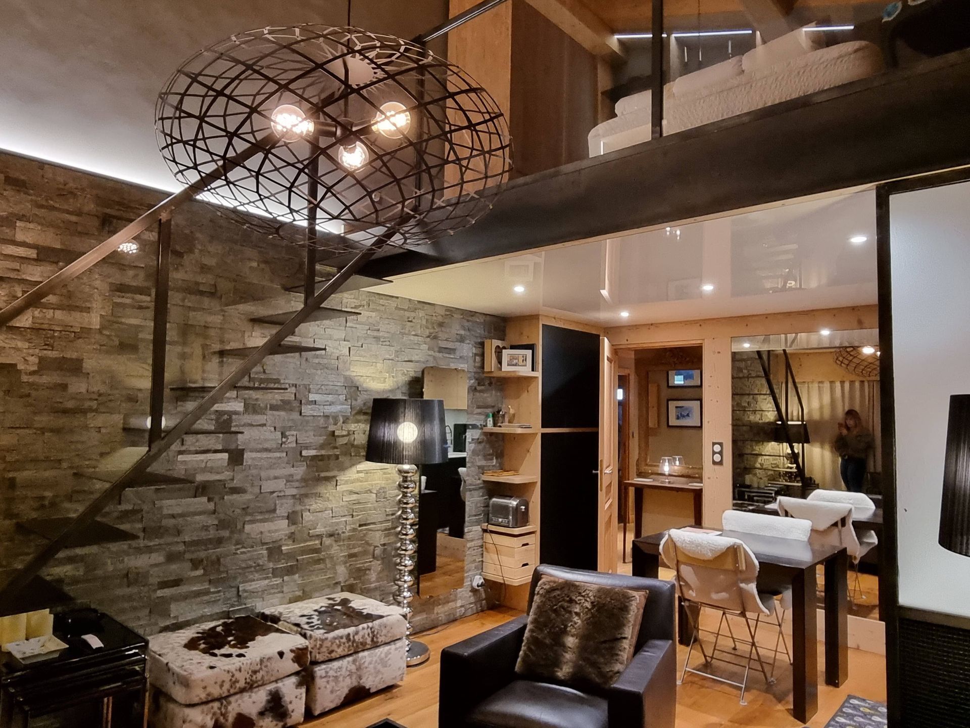 Intérieur d'un loft avec mur en pierre, escalier en métal et mobilier moderne.