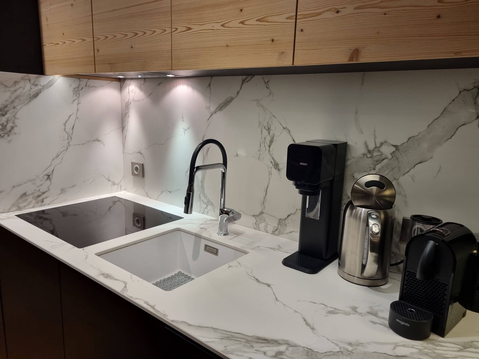 Coin évier de cuisine moderne avec comptoirs et crédence en marbre, éclairage sous les armoires et machines à café.